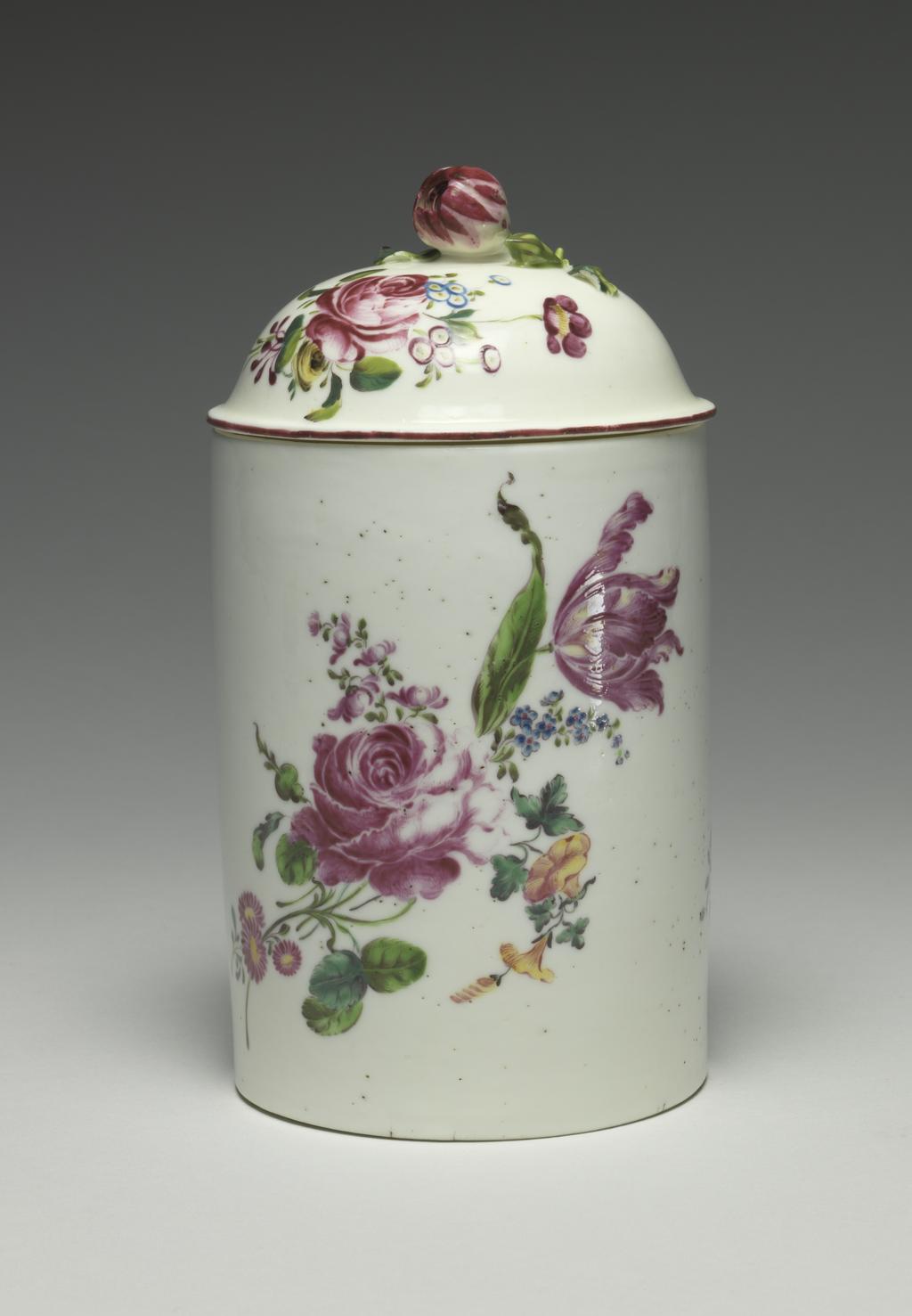 An image of Tobacco jar and cover. The cover may be a 'marriage'. Mennecy Porcelain Manufactory. Cylindrical with recessed base, and domed cover, with an unglazed flange which fits inside the jar, and an applied knob in the shape of a rose bud, a smaller undeveloped bud, and three leaves on a stalk. The jar is decorated with one large floral spray comprising a tulip, a rose, forget-me-knots, convolvulus and pink daisies, and four smaller floral sprays. The cover is decorated with one large and one small floral spray, and has a dark puce band round the outer edge. Soft-paste porcelain, thrown, lead-glazed, and painted overglaze in blue, green, yellow, and rose-pink enamels, height, whole, 16.4 cm, height, jar, 11.9 cm, diameter, jar, 8.7 cm, diameter, cover, 9 cm, circa 1750- 1760. Rococo.