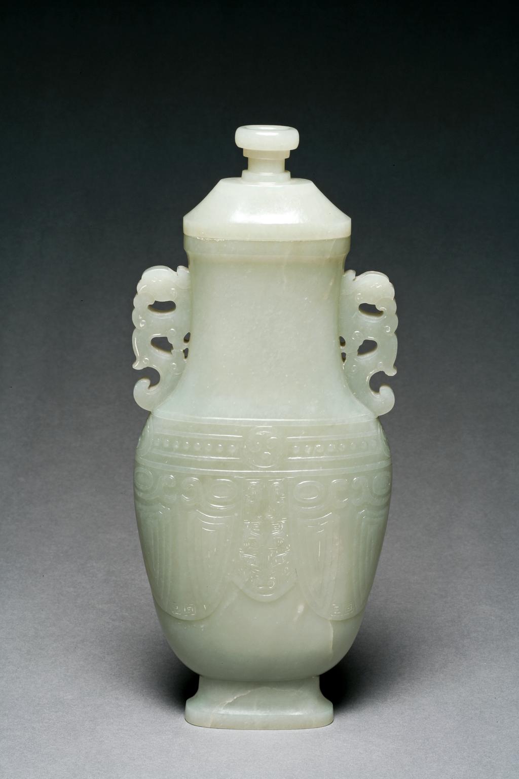 An image of Vase. Pale green jade flattened baluster jade vase, the body decorated with an archaistic taotie face between two cicada. The neck set with phoenix handles and a band of roundels and beads decorated below. nephrite, height, with lid, 24.7 cm, width 11 cm, 1750-1800. Chinese.