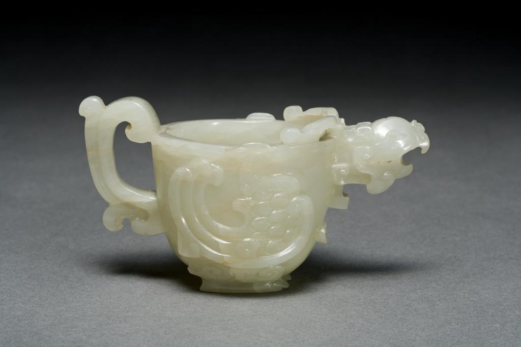 An image of Water dropper. Pale grey jade water dropper in the shape of a cup. The spout is designed as a head of phoenix with a perforation. The main body of this cup is designed as a bird’s wings and the base as bird’s feet. Nephrite, height 5.1 cm, width 10.2 cm, 1750-1800. Chinese.