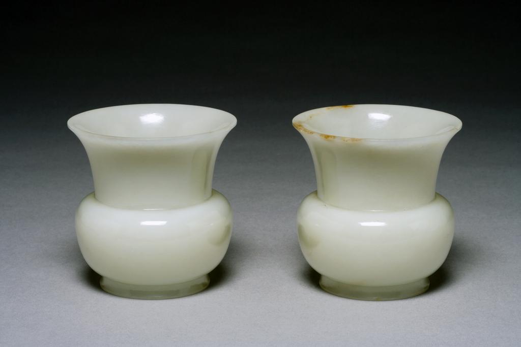 An image of Spittoon/Zhadou. White jade with brown areas on the rim, softly polish, well hollowed with the straight sides flaring out from the flat base before stepping sharply in at the shoulder and flaring out again to the wide trumpet mouth. Nephrite, height 8.5 cm, diameter, mouth, 8.5 cm, 1700-1800, Chinese.
