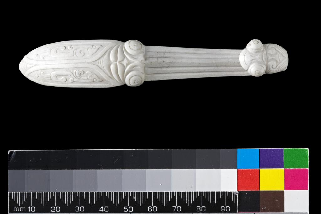 An image of Belt hook/dai gou. Opaque white jade with grey line inclusions. The body decorated with a cicada with a phoenix motif on its wings. The hook terminates with a praying mantis with prominent eyes. The topic of this carving refers to the well-known proverb: When the praying mantis is (intent on) catching the cicada, it fails to notice that the yellow bird is behind (waiting to catch the praying mantis). Nephrite, length 11.1 cm,1600-1800, Chinese.