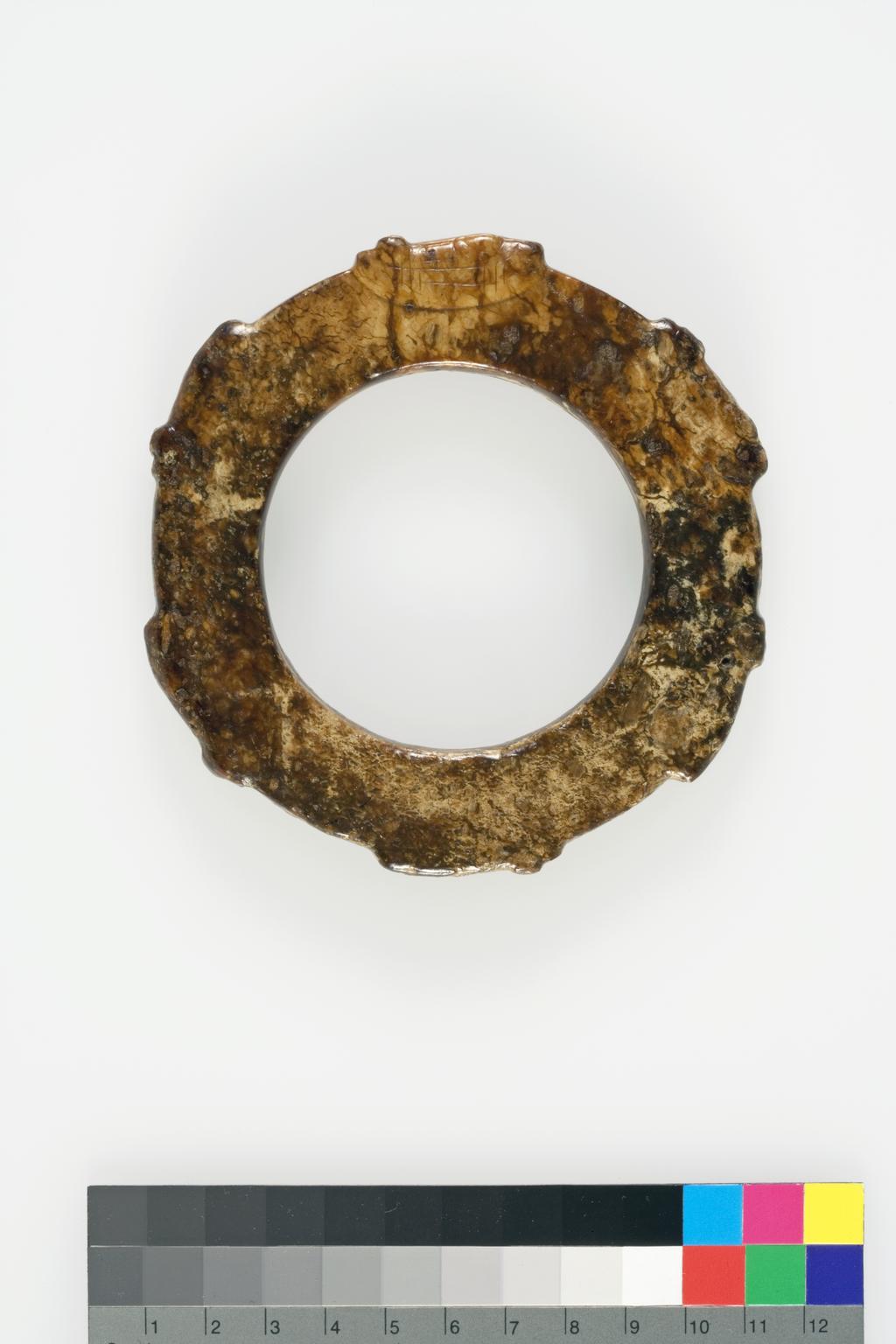 An image of Bracelet. This bracelet is dark brown opaque stone with areas of russet, grey and yellow. Six semi-circles in relief embrace eyes, perhaps representing cicadas enliven the surface of this bracelet. However, it was copied from an early 20th century print Tao zhai gu yu tu (Ancient Jade Illustrations from the Tao’s Studio by Duan Fang, 1861-1911). Nephrite, diameter, 10.8 cm, 1850-1900. Chinese.