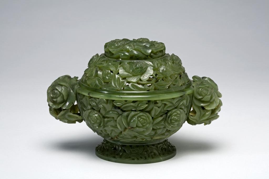 An image of Pomander. Dark spinach green jade, carved and pierced with full-blown peony flowers and foliage. The base flanked by two peony head handles and the domed cover surmounted by three openwork peonies. The openwork design suggests that it was used for non-burning incense or aromatic substances, such as dried flowers. Nephrite, height 9.8 cm, length, including handles, 15 cm, diameter 10.2 cm, 1736-1795 AD. Chinese.