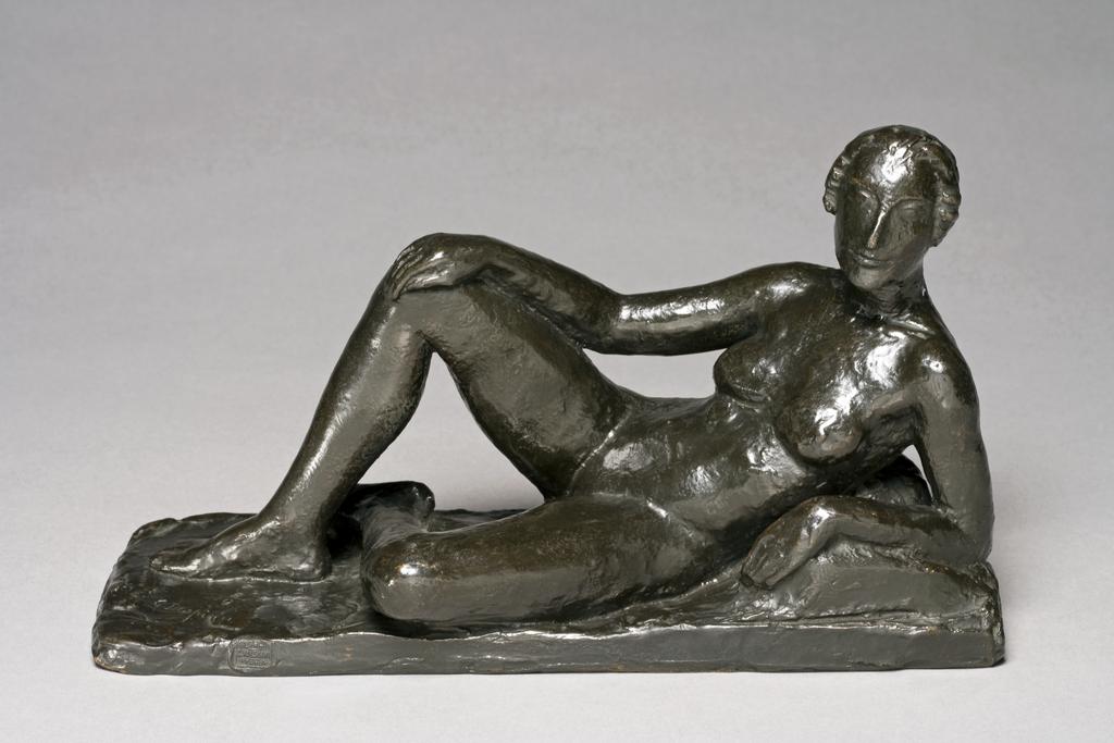An image of DESPIAU, Charles'Reclining Female Nude'Bronze, cast, with dark brown patina, slightly polished.. The reclining figure rests on her left elbow; the right knee is raised and the right hand and arm rest on it; the left leg, flat on the ground, is crossed under the other. The left elbow is raised on a pillow. The figure is attached to its base.FranceC.1922