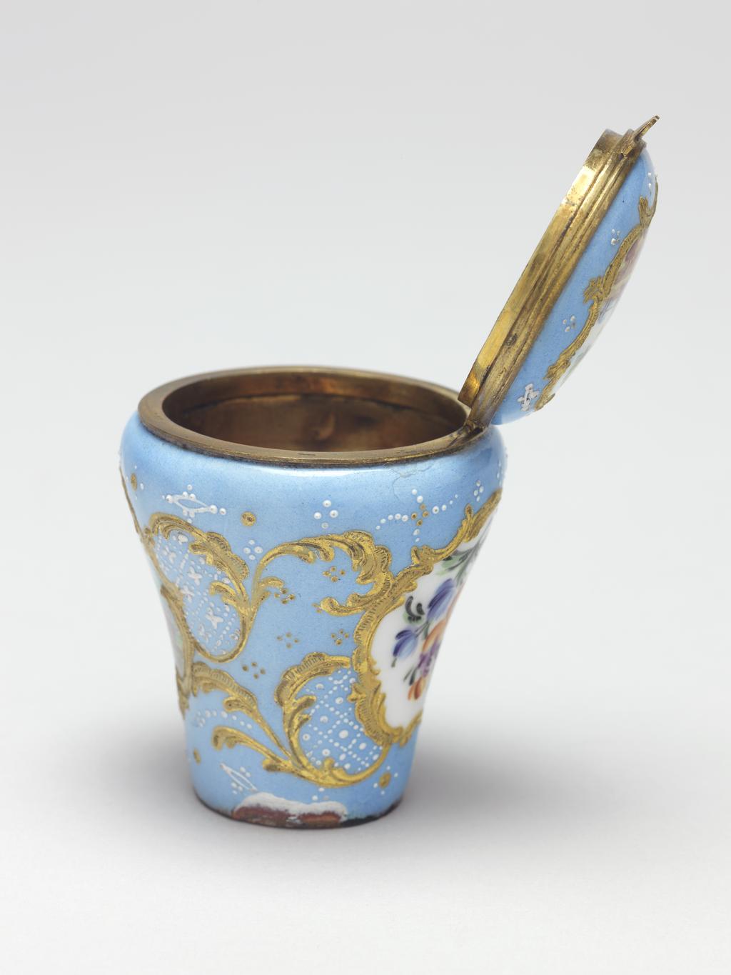 An image of Cane Handle/Snuff Box. Objets de vertu. Unknown maker, Staffordshire. Baluster-shaped handle for a walking cane set with a hemi-spherical gilt metal snuff box with a hinged lid. On two sides and the lid are painted miniatures within rococo raised gilt borders. The pale blue ground decorated with white diaper-work and geometric patterns of gold and white dots. The rim of the lid and box have gilt metal mounts and thumbpiece. The miniature on the lid depicts a Classical ruin in a pastoral scene; the miniature on the front depicts a man and cow in a rural landscape with a church tower and cottage in the background, and the miniature on the back depicts a spray of flowers on a white ground. Copper, enamelled in polychrome, with gilt metal mounts, height, whole, 5.5 cm, diameter, whole, 4.5 cm, circa 1750-1775.