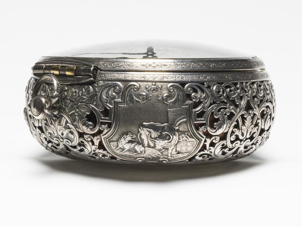 An image of Verge alarm coach watch. Movement: Thomas Windmills, London, c. 1725; case probably by Sarah Jaques and John Lee, London. Movement: brass, silver and steel, engraved ‘Thomas Windmills LONDON 7303’. Dial: silver champlevé with blued steel hour and minute hands. Case: silver, pierced and chased with four repoussé panels from Aesop’s Fables. Interior stamped with maker’s mark incuse ‘SI IL’. Case: height 13.9 cm, diameter 12.6 cm, depth 6.1 cm, circa 1725. London. 