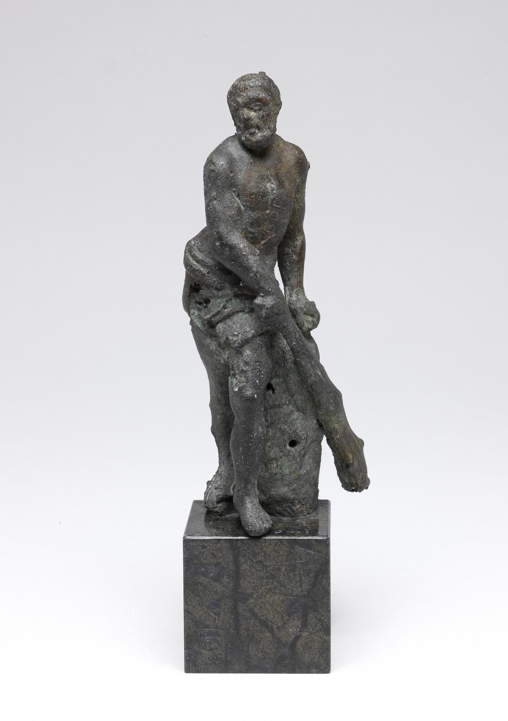 An image of Sculpture/figure. Hercules. Unknown maker, Florence. Hercules stands on his right leg with his left leg advanced. His right arm is held across his body, the hand grasping a club. His left hand rests on the top of a tree stump. There is a drape around his hips. Bronze, cast, standing on a green and black marble base, height, whole, 16.1 cm, circa 1670-1700. Production Note: Bronze, a casting disaster. It is of interest due to this fact.