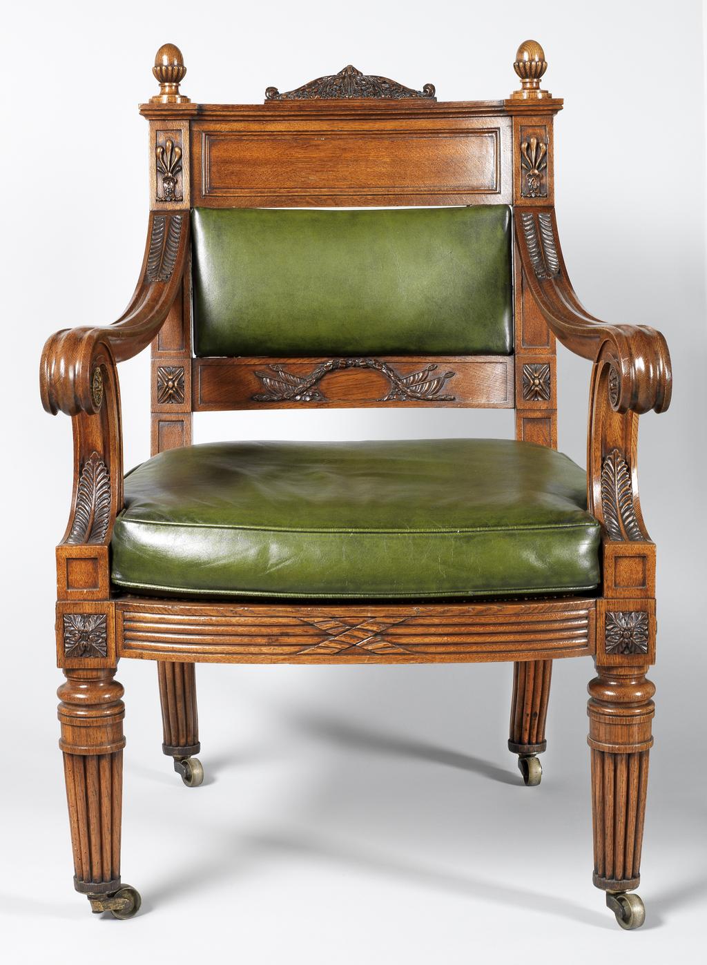 An image of Furniture. Chippendale, Thomas II, attributed to (British, 1749-1822). Armchair of carved oak with turned legs and caned seat, with modern green leather squab seat cushion and back panel and brass casters. Replacement back and cushions, Old woodworm holes. Oak frame, cane seat, leather back panel, cushion (replacement), brass (alloy) castors, height, 107.5 cm, width, front, 68 cm, width, back, 57 cm, depth, 64.2 cm, circa 1820 to circa 1821. Regency Period. Production Note: The design is related to three chairs carved from the famous 'Waterloo Elm'. Two were commissioned from Thomas Chippendale by John George Children (1777-1852). The first was given to George IV in 1821 at Carlton House, and is now at Windsor Castle. The second was for Children's own use. It was given by him to the Duke of Wellington in 1837, and now at Apsley House, London. A third armchair was commissioned by the Duke of Rutland, and is at Belvoir Castle. The Fitzwilliam's chair is close in design to the chair at Apsley House.