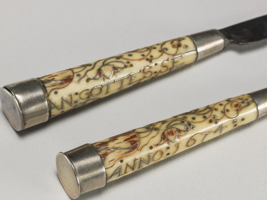 An image of Cutlery/Pair of knives and case. Unknown handle maker and case maker. Unidentified cutler. Object probably either German or English. Ivory, silver, enamel and steel, shagreen and white metal; each knife has a steel tapering blade and ivory handle of circular section with silver ferrule and terminal cap. Both ivory handles are inscribed and decorated with scrolls and tulips in inlaid silver wires and red enamel . Knife A is inscribed 'AN: GOTTES: SE / EN: IST: ALLES' and knife B is inscribed 'GELEGEN / ANNO: 1674'. The case (C) is of wood covered with unpolished pearl ray shagreen with a white metal mount to the tip. It has a pull-off lid, is of lobed oval section and tapers to a point. Length, knife A, 13.5 cm, length, knife B, 13.3 cm, length, case, 17.3 cm, circa 1674. English.