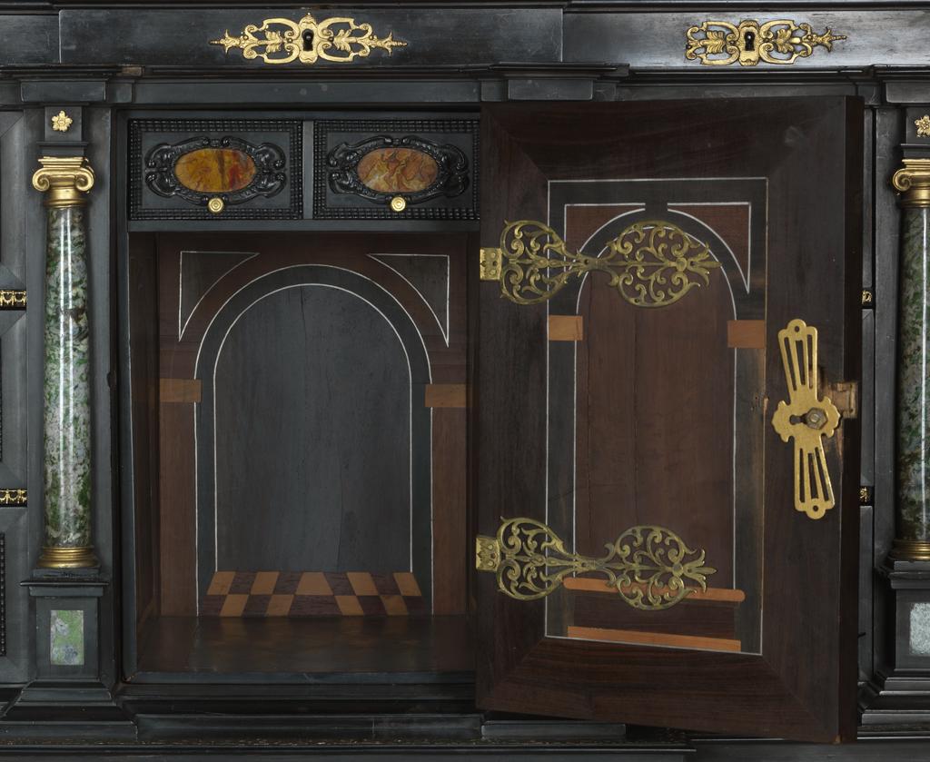 An image of Augsburg 17th century silver-gilt mounted ebony Table Cabinet with Florentine pietre dure plaques from the Grand Ducal workshops. Boscher, Elias (1600-1674). Of architectural form, the stepped superstructure fitted with three frieze drawers above a central cupboard door, architectural pediment and inset with a panel depicting a chaffinch on a fruiting bough, flanked by columns of Smaragdite Gabbro with Corinthian capitals flanked by two deep drawers, inset with panels depicting parrots within fruiting boughs, with three further fitted drawers below, the large central cupboard door inset with a panel of a lapis lazuli flower filled urn issuing stems including a carnation, anemone, daffodil and lilies and enclosing an architectural interior, flanked by further Smaragdite Gabbro Ionic columns and three drawers to each side inset with further symmetrical floral panels including tulips, roses, carnations, lilies and bluebells, on shaped bracket feet, each side inset with large central panels of parrots on fruiting boughs, with four further floral panels above and below, the reverse veneered in kingwood, amaranth and stained walnut in geometric stellar designs. The cabinet containing a complex series of fourty-four secret drawers and compartments to the interior. The cabinet is signed in pencil on the underside 'Elias Boscher' and 'gemacht'. The central cabochon mount stamped with the Augsburg town mark and the silversmiths mark of Johann Spitzmacher (active 1655-1678). The front bears the ebony stamp "EBEN" with the pinecone of Augsburg. Height 85 cm, width 84cm, depth 40cm, circa 1660.