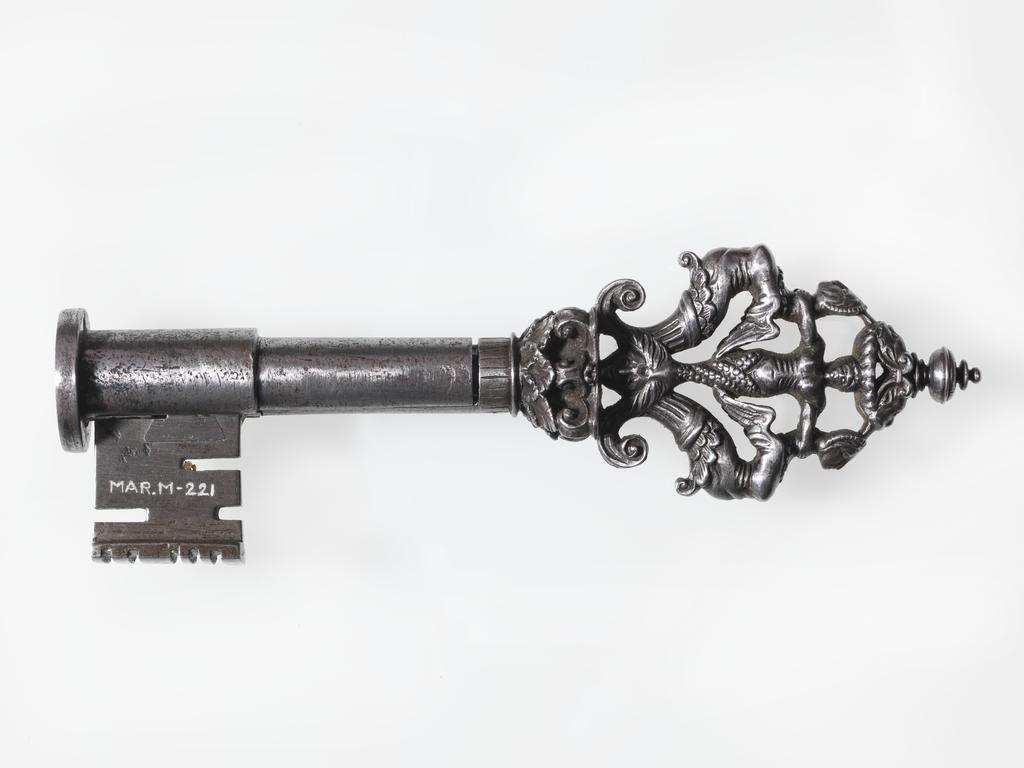 An image of Key. Iron, with piped stem, spade-shaped in section, collar in the form of a capital of Corinthian type and bow composed of two winged grotesque female figures back to back with a mermaid between them. Circa 1500-1600. French. Notes: Has cover for the stem.