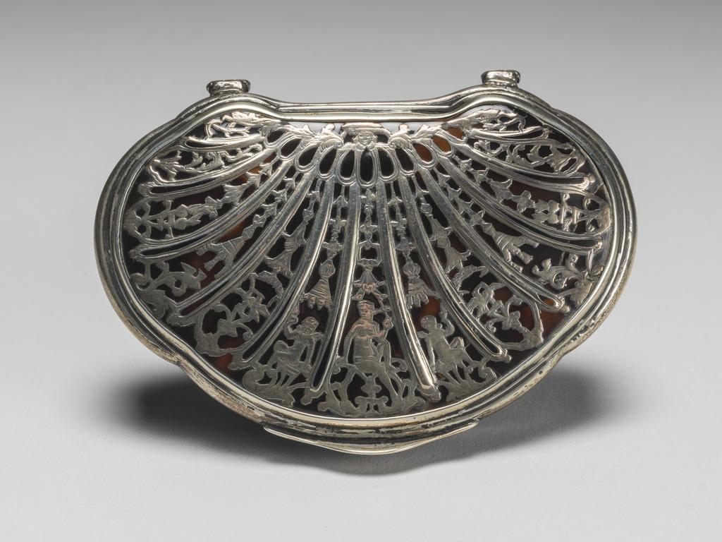 An image of Snuff Box. Objets de vertu. Unknown, maker. The silver does not bear a maker's mark or hallmarks. Shell-shaped with straight sides. The slightly domed lid has stepped silver mounts, two projecting hinges and an arched thumbpiece. The top is decorated to resemble a shell with twelve ribs dividing the surface into thirteen panels. These contain stylised pendant flowers and, in the centre, a naked woman with a cherub on either side. On the base is an impressed plant shape, which would originally have contained a silver piqué ornament. The tortoiseshell was carved from a turtle shell, which was heated and pressed to form the parts of a box, which were glued together. The silver mounts were fitted round the rim of the box and the two hinges were attached with screws. The silver piqué was inlaid and engraved. Height, whole, 1.9 cm,  length, whole, 9.3 cm, width, whole, 6.8 cm, 1710-1740.