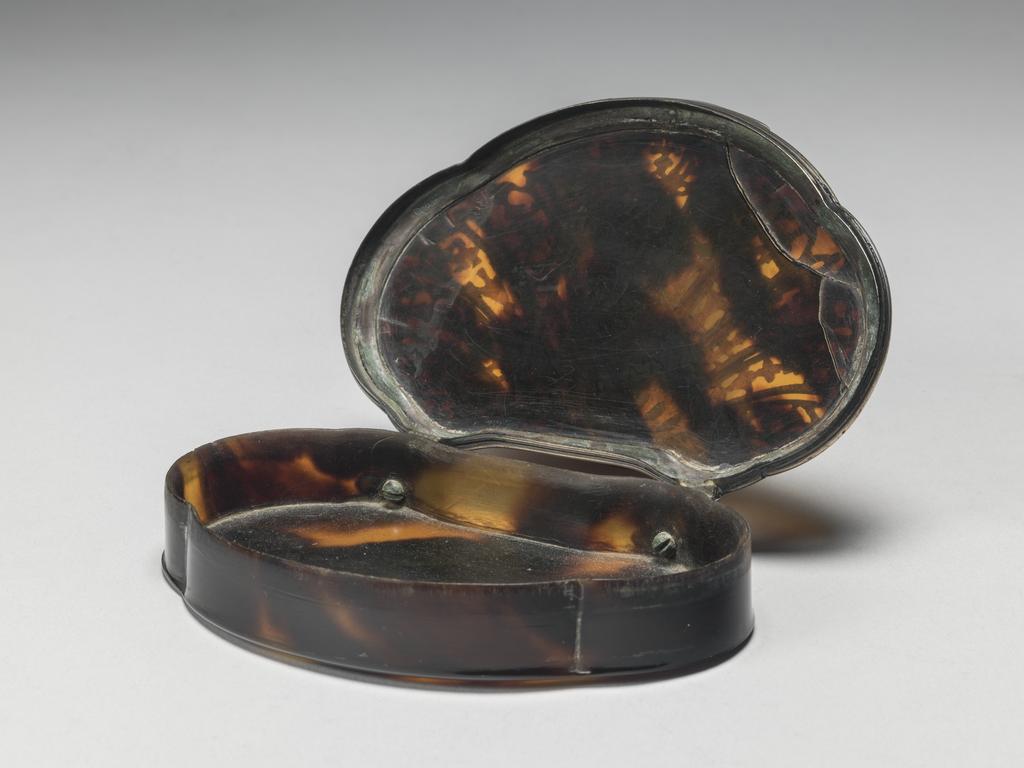An image of Snuff Box. Objets de vertu. Unknown, maker. The silver does not bear a maker's mark or hallmarks. Shell-shaped with straight sides. The slightly domed lid has stepped silver mounts, two projecting hinges and an arched thumbpiece. The top is decorated to resemble a shell with twelve ribs dividing the surface into thirteen panels. These contain stylised pendant flowers and, in the centre, a naked woman with a cherub on either side. On the base is an impressed plant shape, which would originally have contained a silver piqué ornament. The tortoiseshell was carved from a turtle shell, which was heated and pressed to form the parts of a box, which were glued together. The silver mounts were fitted round the rim of the box and the two hinges were attached with screws. The silver piqué was inlaid and engraved. Height, whole, 1.9 cm,  length, whole, 9.3 cm, width, whole, 6.8 cm, 1710-1740.