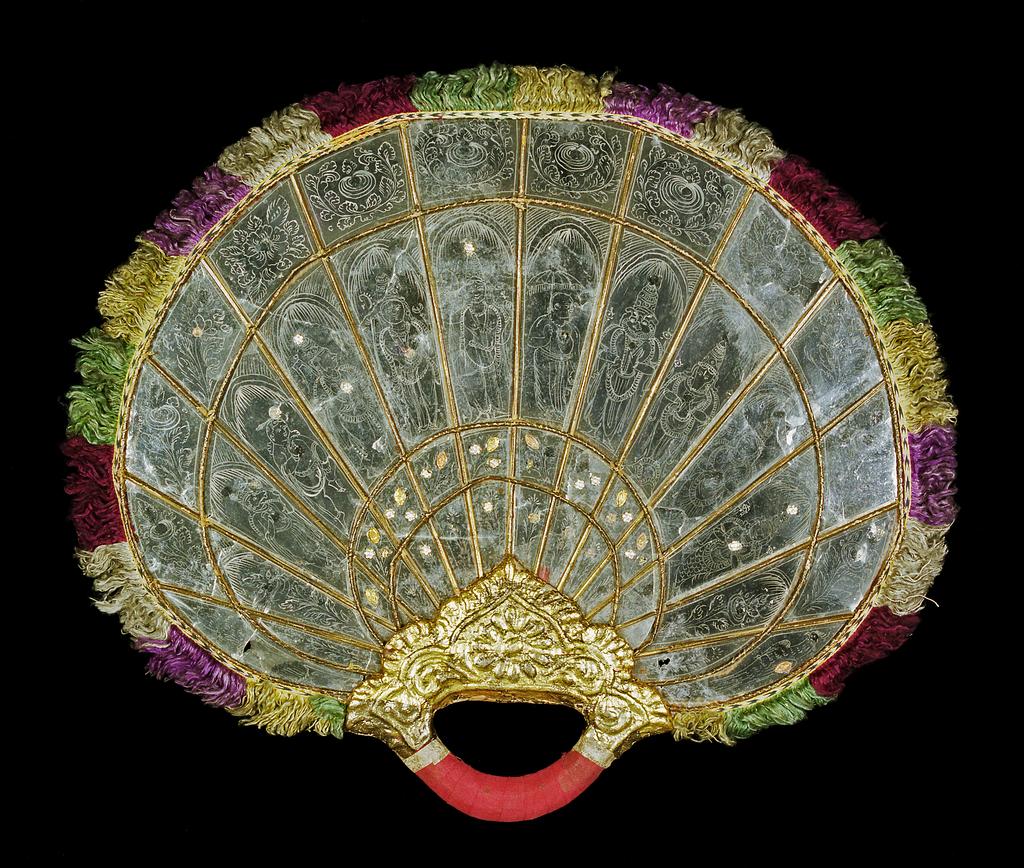 An image of Fans. Fixed fan with loop handle, decorated with Hindu deities. Production Place: Probably Southern India. Mica, painted white with applied gilt and silver 'jewels', mounted in cane; the handle is moulded and gilt and bound in red cotton; silk fringe in white, red, green, yellow and blue. Height, whole, 38.1 cm, width, whole, 44.6 cm, after 1801 to before 1900. Messel-Rosse Collection.