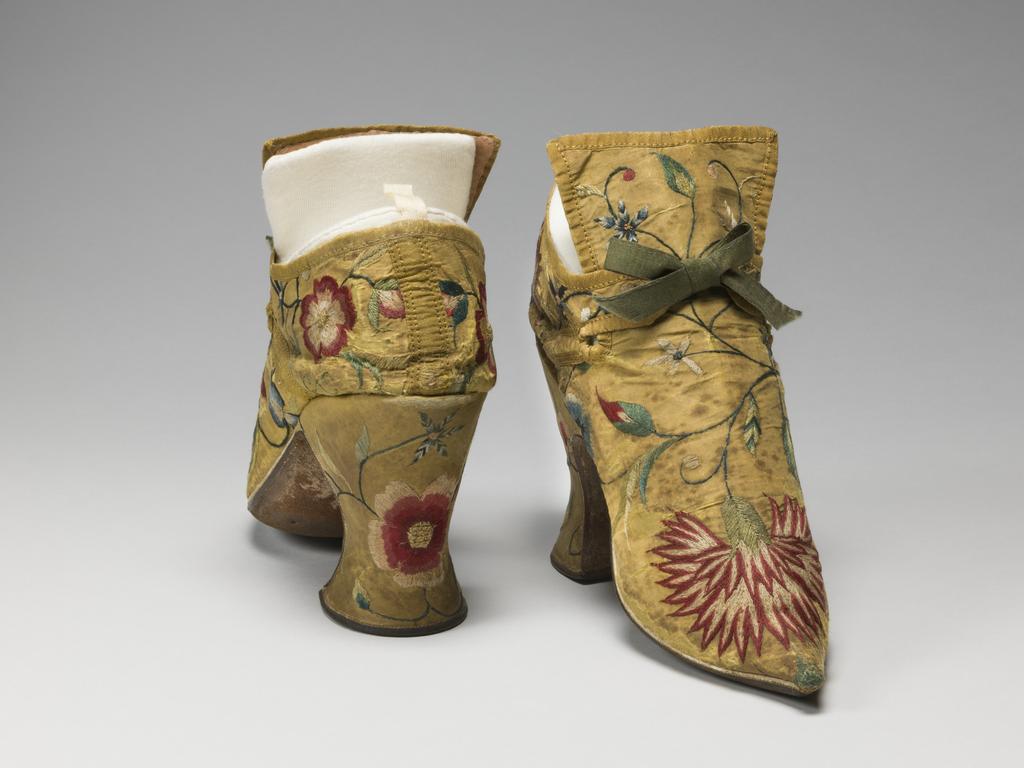 An image of Textiles. Shoes/pumps. Silk taffeta, bound with ribbon; floss silk embroidery in French knots, long and short, satin and split stitches; tied with ribbon. Ground covered by a pattern of trailing and scrolling stems with leaves and flowers, carnation, rose, etc., so arranged that there is a carnation on each toe and a rose on each heel with a five petalled blue flower above it. The left shoe has a rose, the right a carnation at each side of the seam. Silk, length, whole, 7 in, height, back, 5.25 in, height, heel, 3 in, circa 1700-circa 1749. English.
