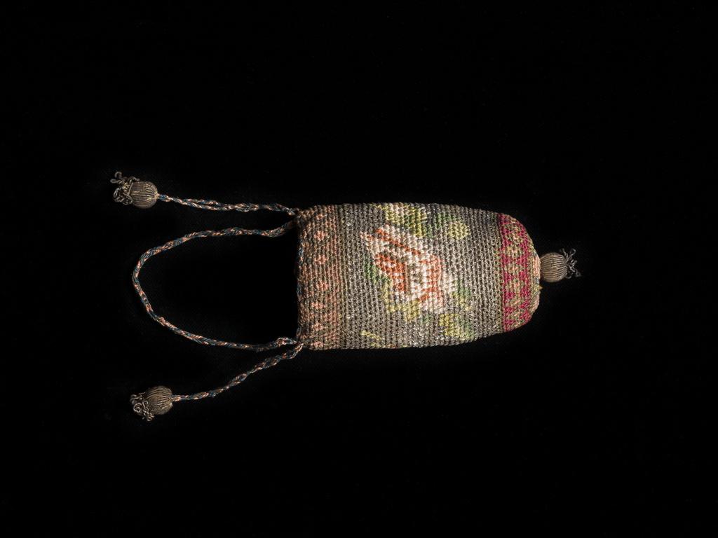 An image of Textiles. Purse. Buttonhole stitch worked spirally on a cone shaped mould; two stitches are worked into the interspace between the stitches of the previous row. Colours brown, green and pink. At the bottom is a five-pointed star, above it a band of lozenges, gold with a pink centre upon a red background. At the top a similar band of lozenges but the background a pinkish brown. The background of the main body of the purse is silver thread with two rose sprays each consisting of a rose, a bud and leaves. The draw strings are formed by a plait of silver thread and pink and blue silk; the tassels are a large and small spherical bead covered with silver bullion. Silk, with gold and silver thread, length 3.75 in, diameter 1.75 in, circa 1600- circa 1699. English.