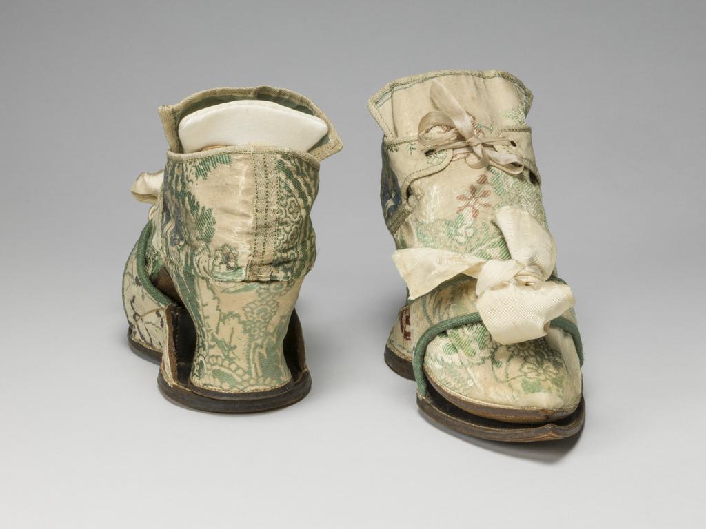 An image of Textiles/Shoes and pattens. Brocaded silk, cream background, multicoloured floral design. Shoes lined with coarse linen, tongues with green sarcenet, bound green braid. Pattens lined scarlet flannel, bound green braid, cream corded silk bows, leather soles and heels. Length, whole, 8.25 in, circa 1700-1749. English.