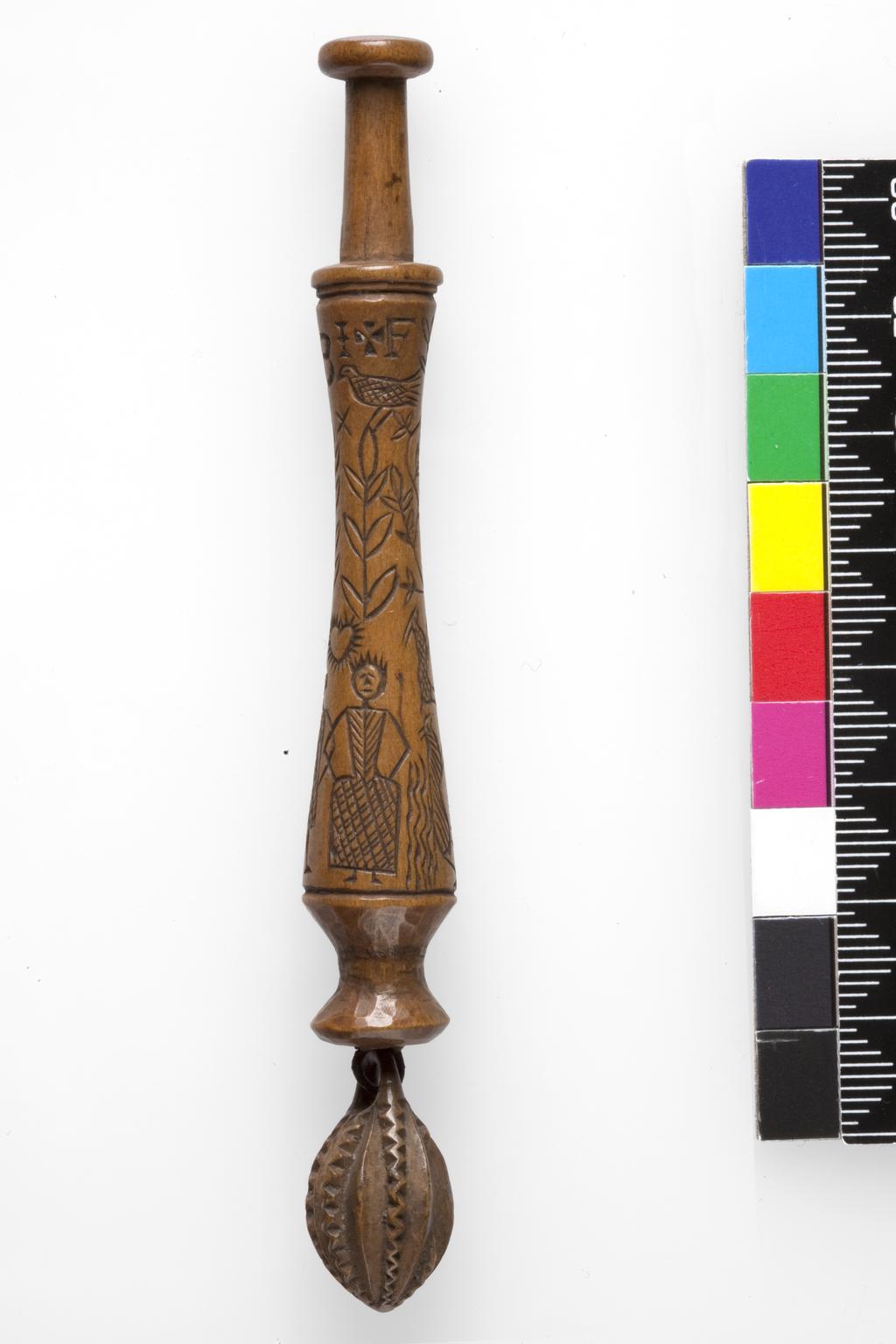 An image of Lace Bobbin. Unknown maker, Bedfordshire, Dunstable Downs. Wood, carved with figures (maker and his wife), sheep, (his) dog, bushes and the sun, moon and stars. Circa 1795. No dimensions.