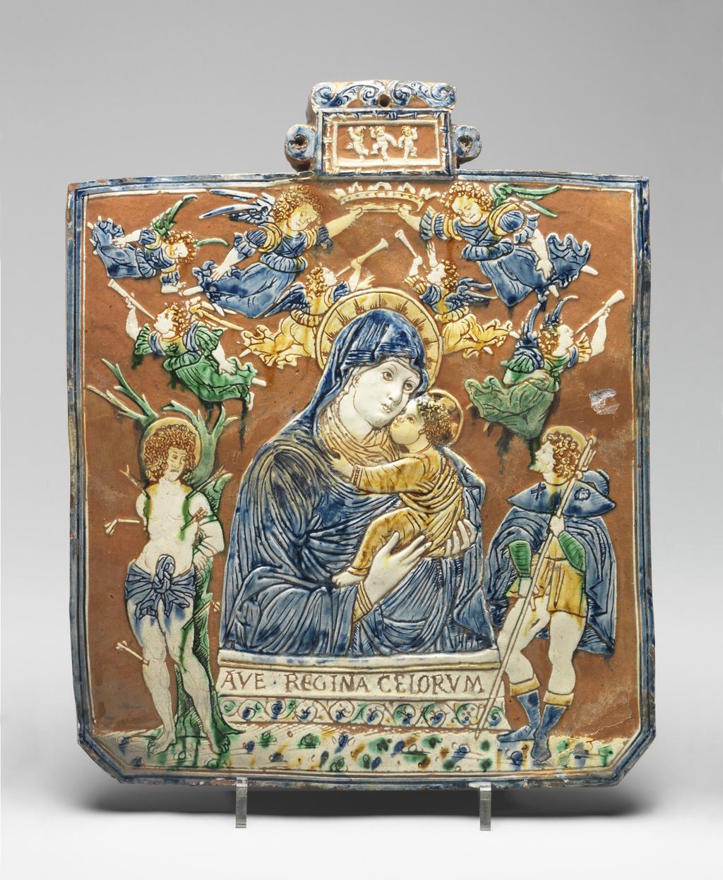 An image of Panel. The Virgin with Saints Roch and Sebastian. Unknown, perhaps The Veneto. Almost square with cut lower corners and a rectangular, scrolled protrusion at the top, with lateral rings and a hole for suspension. A half-length figure of the Virgin holding the Christ Child in her arms, with below, a pedestal inscribed 'AVE.REGINA CELORVM' (Hail Queen of the Heavens), and above, seven angels, of whom two hold a crown over her head and four blow trumpets. St Roch stands on the right hand and St Sebastian on the left. The small panel at the top contains three dancing putti. Pale red earthenware, moulded in very low relief in the middle, and coated with white slip which has been removed from the background. Incised decoration coloured blue, green and dark yellow under lead glaze. Height, whole, 33.7 cm, width, whole, 27.8 cm, depth, whole, 1.7 cm, circa 1500-1510. Renaissance.