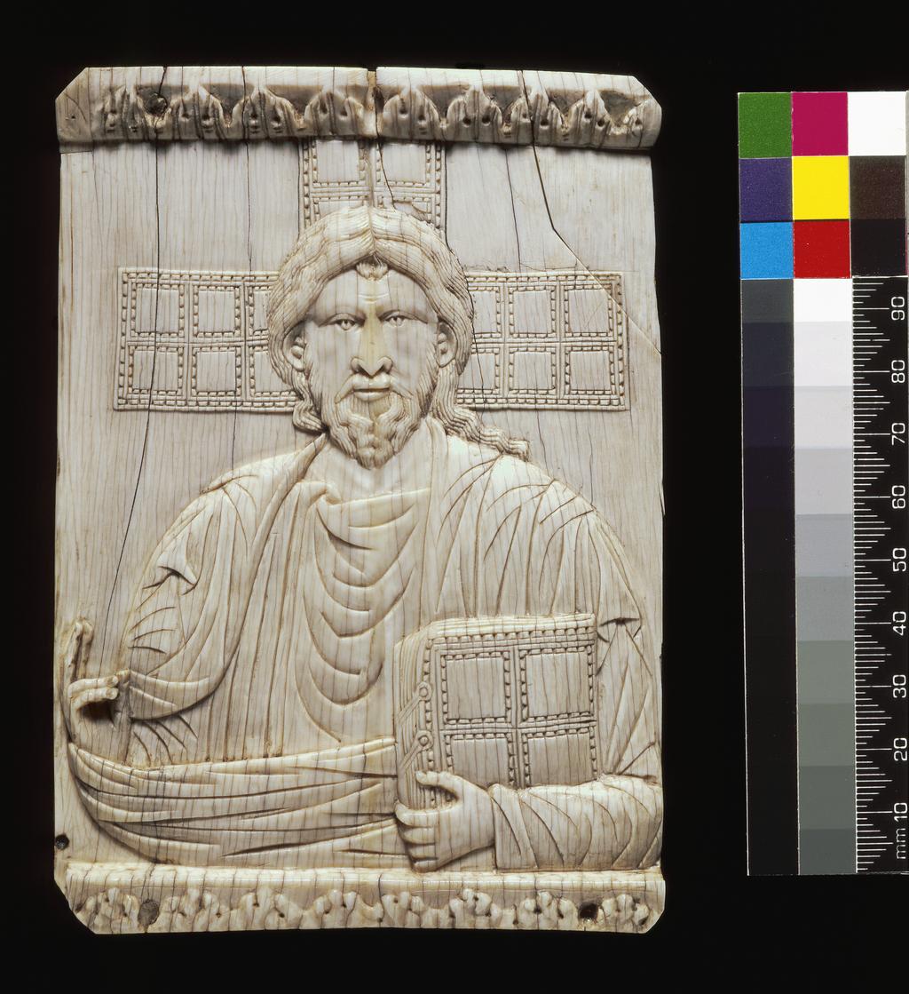 An image of Sculpture/Panel. Christ Pantocrator represented half-length and full-face. Christ holds a book in his left hand and blesses with his right. Behind is seen the three upper limbs of the cross, the surfaces chequered in the same way as the book in Christ's hand. It is from the modern cover of a 10th century lectionary written at Reichenau. Height 138.0 mm, width 97.0 mm, circa 900 to 1000. Production Place: Byzantium.