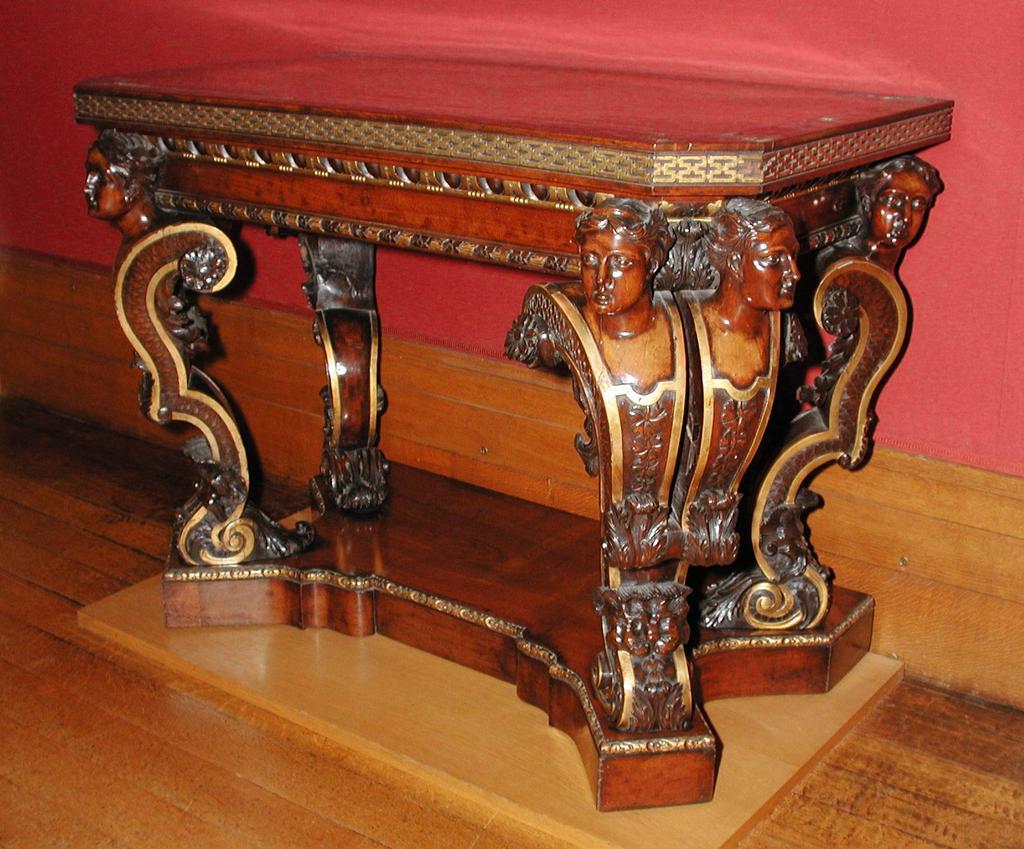 An image of Furniture. Side table/pier table/console table. Carved and partly gilt mahogany console table. The top is inlaid with brass banding of interlacing ribbands enclosing floral quatrefoils. Supported on six scrolling female-headed terminals rising from a shaped base. Mahogany, brass (alloy) inlay, gilt, height 84.6 cm, length 111.8 cm, depth 63.5 cm, circa 1730. George II.