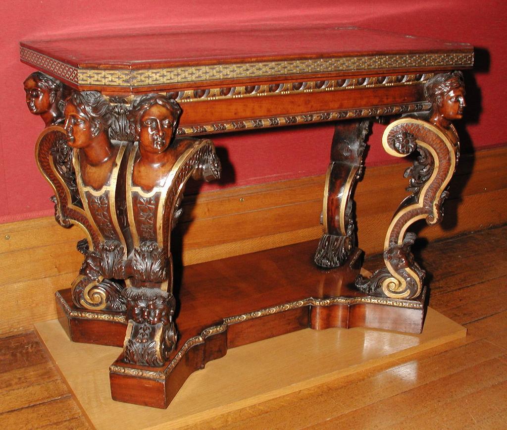 An image of Furniture. Side table/pier table/console table. Carved and partly gilt mahogany console table. The top is inlaid with brass banding of interlacing ribbands enclosing floral quatrefoils. Supported on six scrolling female-headed terminals rising from a shaped base. Mahogany, brass (alloy) inlay, gilt, height 84.6 cm, length 111.8 cm, depth 63.5 cm, circa 1730. George II.