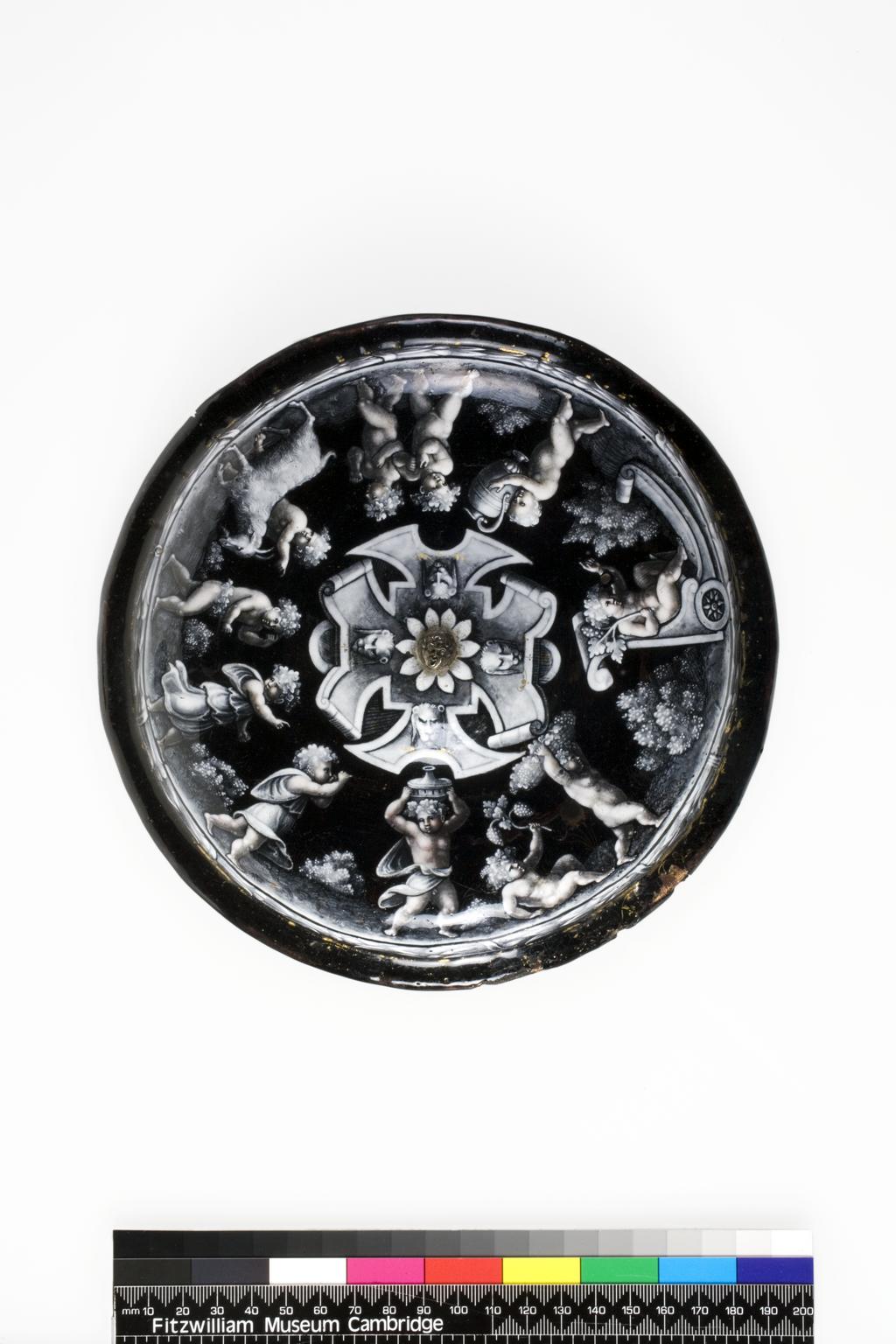 An image of Standing Cup with Cover/Tazza. Master IC (workshop). Court dit Vigier, Jean I (French, workshop, d. 1592). The interior of the cup is decorated with the Creation of Adam. The cover is decorated on the exterior with a central flowerhead surrounded by four leonine masks on curling strapwork, around which is a continuous procession of revelling putti wearing vine wreaths in their hair. The hemispherical bowl of the cup is supported on a vase-shaped knop on top of a bell-shaped circular foot. The low domed cover has a flange round the edge, and a raised central area with a replacement finial in the form of a horizontal metal grotesque mask.Copper, enamelled en grisaille with pink on a black ground. Height, whole, 19.2 cm, height, cup, 15.5 cm, diameter, rim of cup, 17.5 cm, diameter, foot of cup, 10.5 cm, diameter, rim of cover, 19.5 cm, circa 1555- before 1580. Limoges, France. Renaissance.