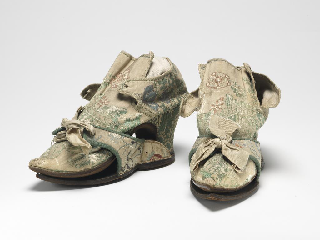 An image of Textiles/Shoes and pattens. Brocaded silk, cream background, multicoloured floral design. Shoes lined with coarse linen, tongues with green sarcenet, bound green braid. Pattens lined scarlet flannel, bound green braid, cream corded silk bows, leather soles and heels. Length, whole, 8.25 in, circa 1700-1749. English.