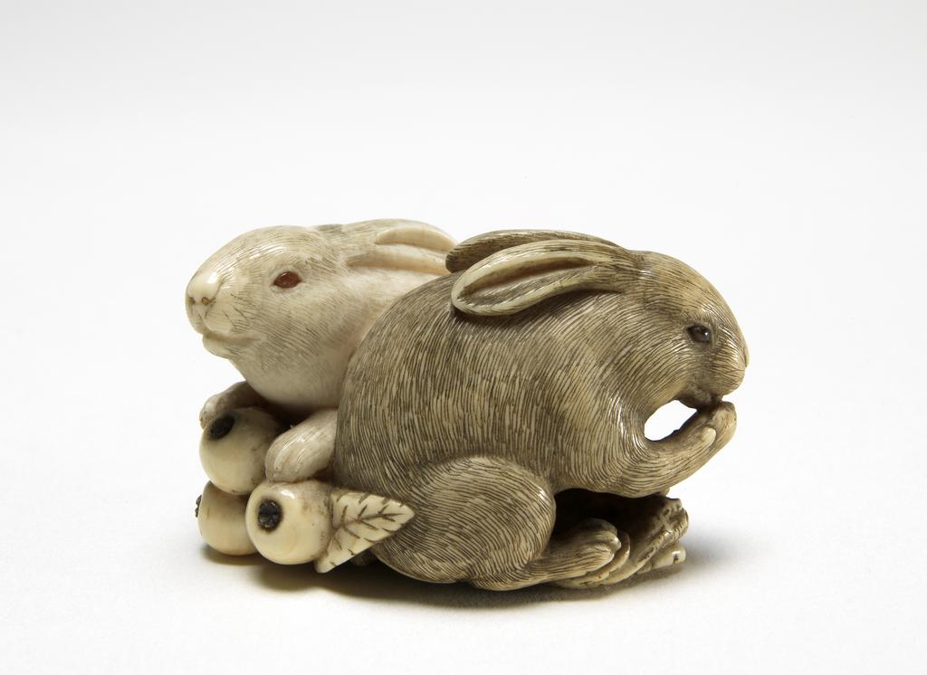 An image of Netsuke. Two rabbits eating loquats. Okatomo (Japanese). Ivory, carved and stained, height 4 cm, width 2.5 cm. Japanese.