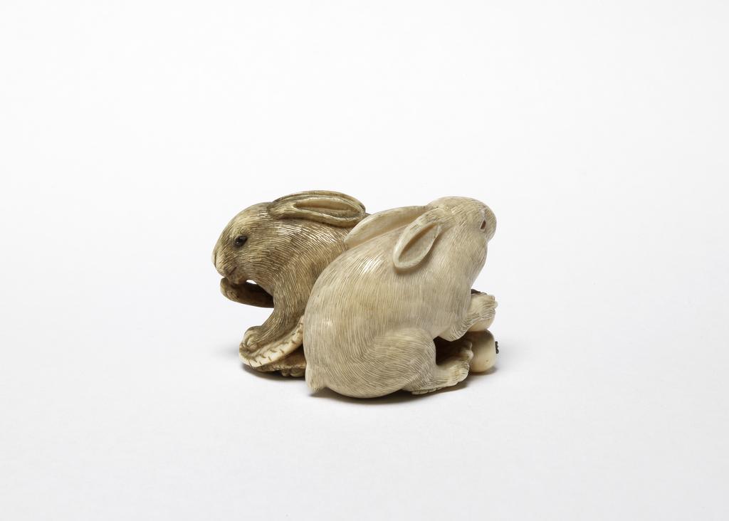 An image of Netsuke. Two rabbits eating loquats. Okatomo (Japanese). Ivory, carved and stained, height 4 cm, width 2.5 cm. Japanese.