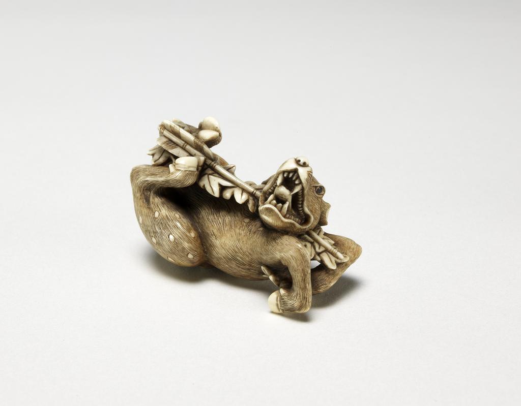 An image of Netsuke. A deer being shot through the jaw by an arrow. Hidemasa (Japanese). Maple leaves attached to the arrow. Illustration of the story of Rokusonno. Ivory, with carved and stained detail, width 5 cm. Japanese.