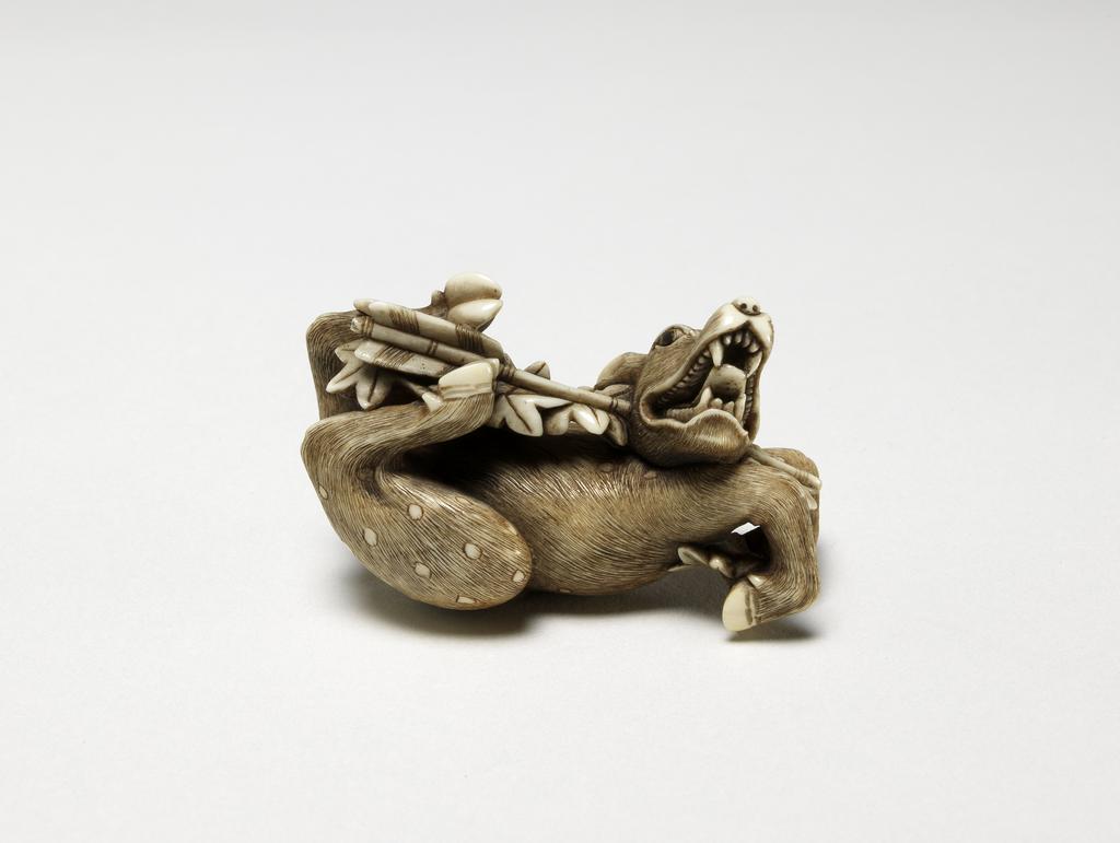 An image of Netsuke. A deer being shot through the jaw by an arrow. Hidemasa (Japanese). Maple leaves attached to the arrow. Illustration of the story of Rokusonno. Ivory, with carved and stained detail, width 5 cm. Japanese.