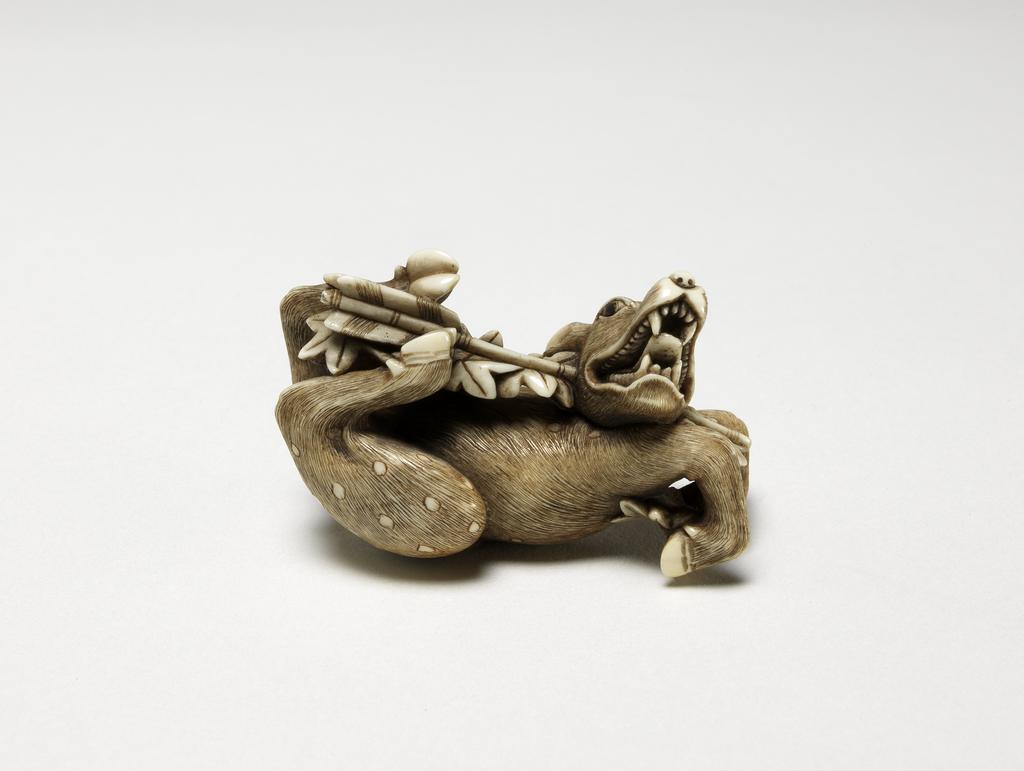 An image of Netsuke. A deer being shot through the jaw by an arrow. Hidemasa (Japanese). Maple leaves attached to the arrow. Illustration of the story of Rokusonno. Ivory, with carved and stained detail, width 5 cm. Japanese.