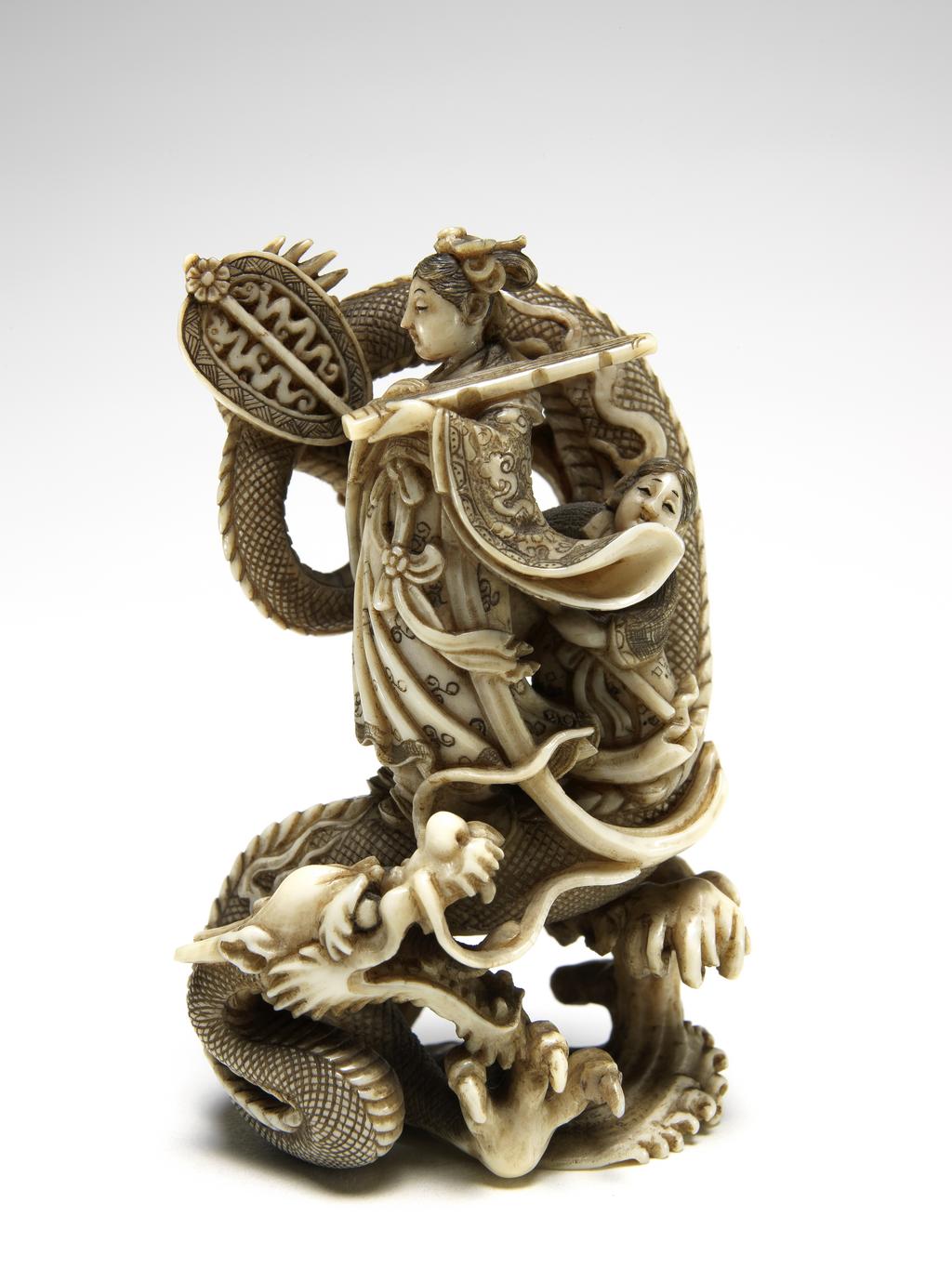 An image of Netsuke. Seiōbo, Queen Mother of the West, crowned with a dove and wearing a cloud and dragon patterned robe. Gyokushu (Japanese). Her attendant holds a fan and they are both standing on a three clawed dragon amongst waves. Middle of fan pole broken. Ivory, height 5.5 cm, width 3.5 cm, c. 1950. Japanese.