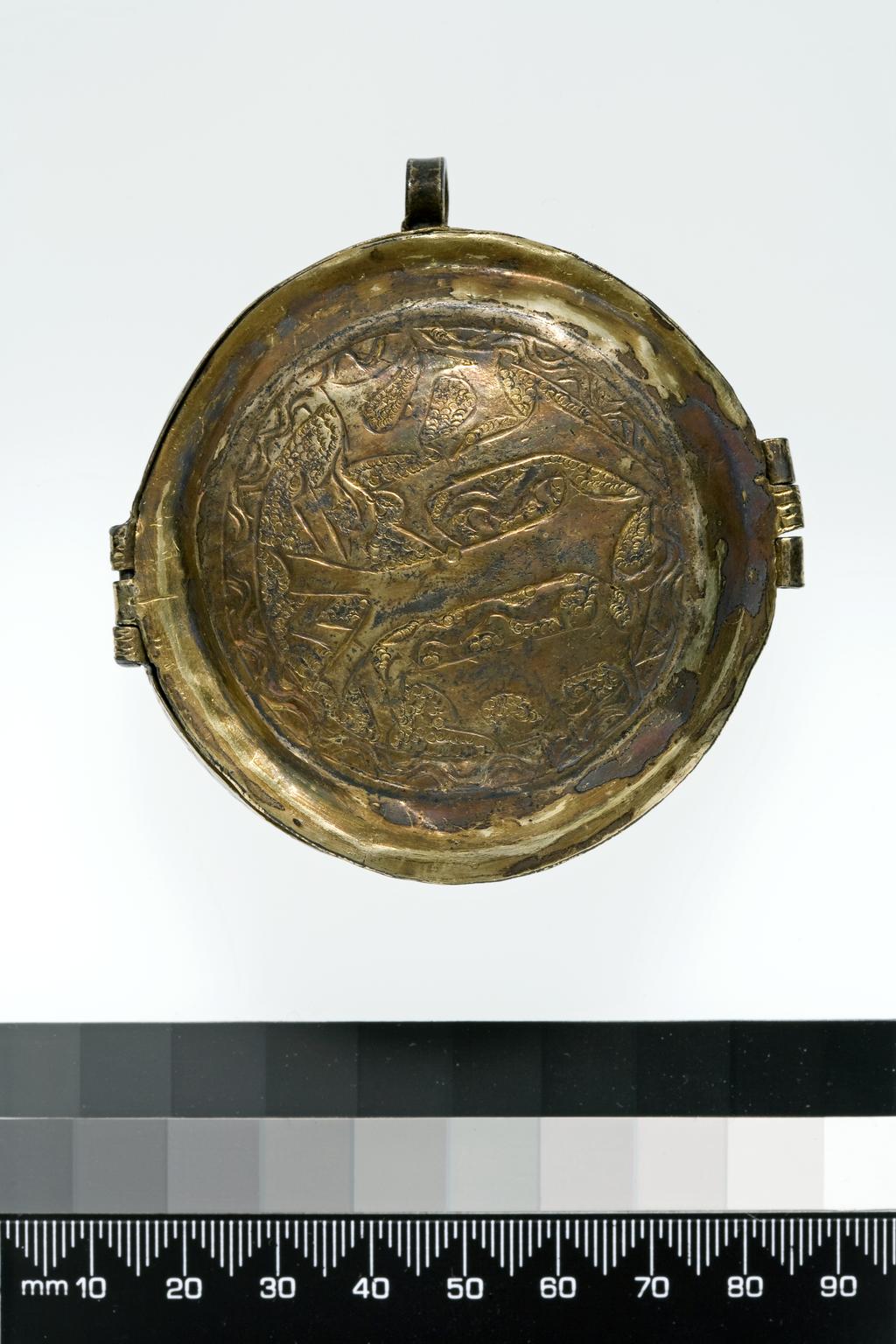 An image of Boxes/Pyx. Church Plate. Sacramental wafer box or reliquary (possibly). Circular with straight sides and slightly domed base and hinged cover. Sacred Monograms are chased on the lid, 'IHS', and the base 'XPS'; both are on a punched scale-work ground and within a chased wavy border. On the opposite side to the hinge is a simple catch of similar form to the hinge with three knuckles. Set at right-angles to the hinge and catch a ring is soldered to the side. Siver-gilt, punched and chased, height 2.6 cm, length 7.6 cm, width 7.2 cm, 1500-1525.