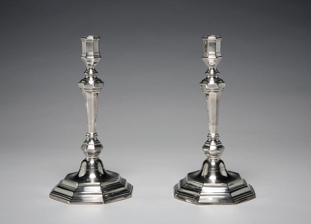 An image of A pair of candlesticks. Grebeude, N., silversmith, France, Paris, Colmar. Of octagonal form. The urn-shaped sconce on a slender vase-shaped column over a flattened knop, stands on a slightly domed base with stepped octagonal foot. Silver, cast, height, overall, 25.2 cm, width, base, 13 cm, weight, whole, 595 g, 1723-1724. Régence. Louis XV.