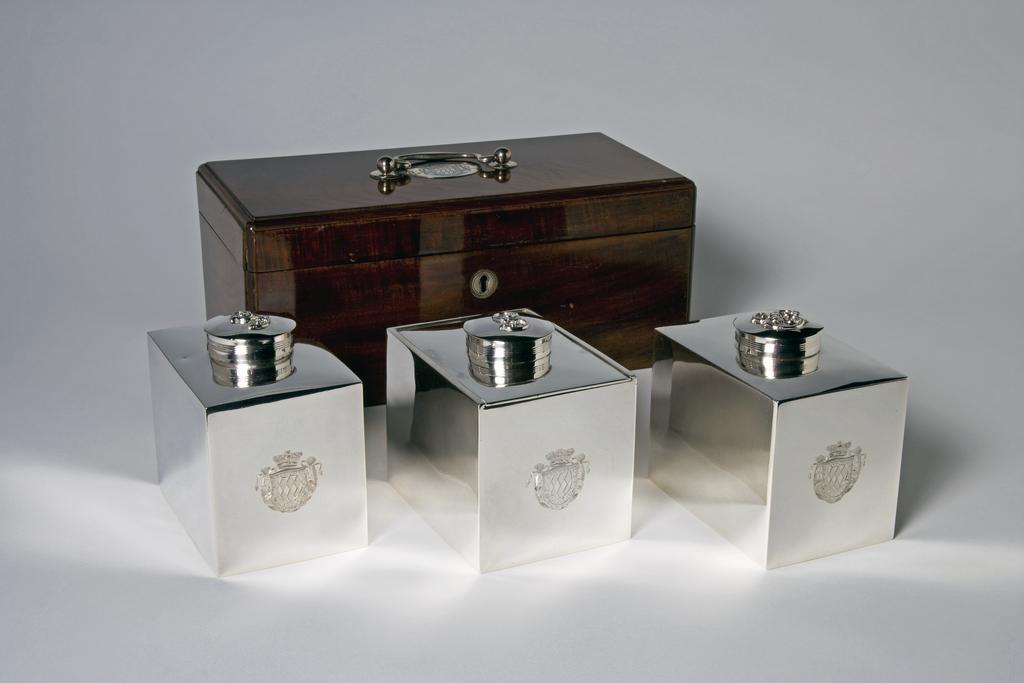 An image of M.7.1 & A-1965, M.7.2 & A & B-1965 and M.7.3 & A-1965. A cased set of two tea caddies and a sugar box. Thompson, William II, silversmith, probably (English). Production Place: England. The rectangular box with silver handle and oval mount engraved with the coat of arms of Richard, 7th Viscount Fitzwilliam. Mahogany case with silver handles and mounts, height, overall, 14 cm, length, overall, 32.4 cm, width, overall, 16.5 cm, 1812-1813.