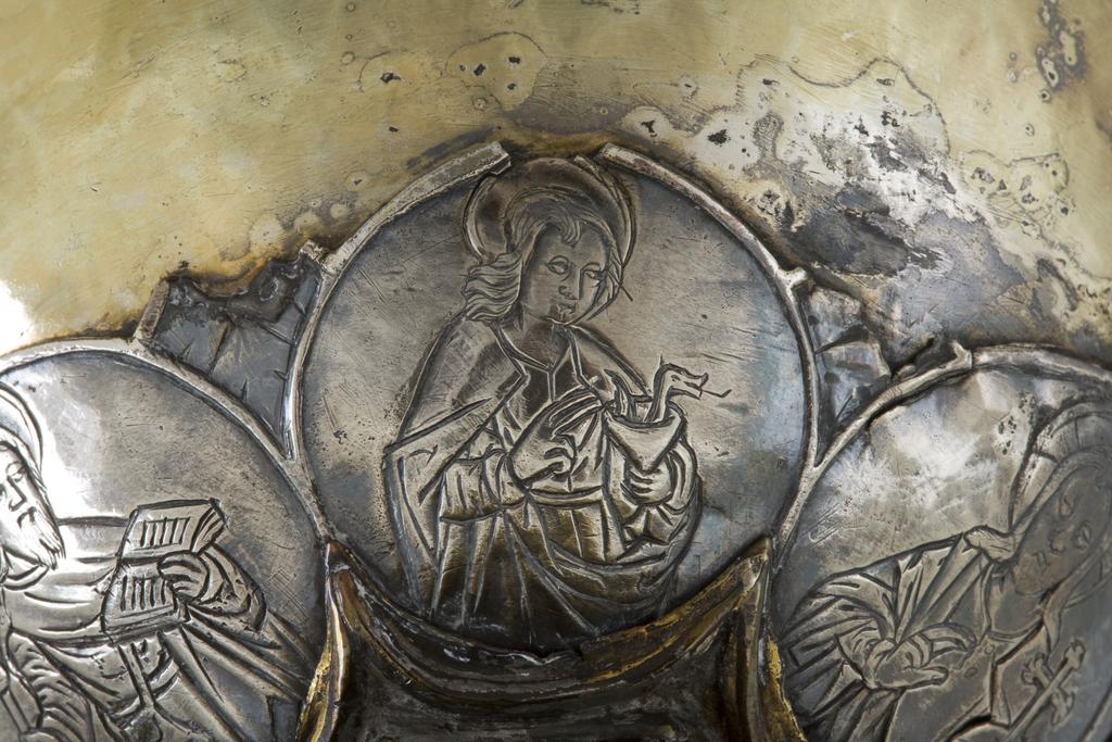 An image of Silver/Church Plate. Chalice. Petruccio Campagnini, Andrea, probably (active Tuscany, Siena, Italy). Set with six silver medallions of Christ, St Peter, St. Paul, St. John, St. Bartholomew and possibly St. Barnabus. Above the knop the stem is engraved with six male busts without nimbi; below the knop the stem is engraved with six birds. At the base of the stem are moulded borders containing a plain band engraved and enamelled with the inscription 'ANDREA * PETRUCI * DE * SENIS * ME *FECI(T). The low copper-gilt trumpet-shaped foot has a shaped circular spreading base with rim of twelve alternating semicicular and pointed lobes. It is set with six applied silver plaques with translucent enamels on sunk relief, representing the Crucifixion with Instruments of the Passion, on either side of which are the Virgin and St. John; on the opposite side are a bishop with mitre and crozier between a male and female saint. Above are smaller shaped triangular plaques enamelled with the heads of angels; and below are lozenge shaped plaques enamelled with a stylised leaf. The base stands on a foot ring decorated with moulded, beaded and dentil borders. Bowl silver-gilt with silver calyx, foot and stem of copper-gilt, decorated with embossing and chasing, and set with silver plaques with basse taille enamelling, height, overall, 19 cm, diameter, base, 12.8 cm, maximum, diameter, rim, 9.9 cm, circa 1370. Late Medieval. Gothic.