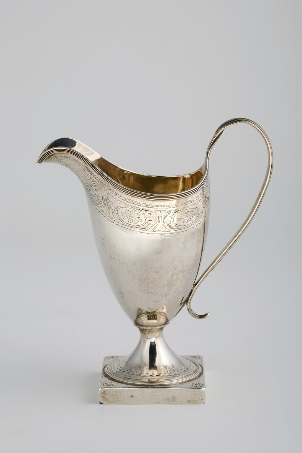 An image of Cream Jug. Bateman, Peter, silversmith, England, London. Bateman, Ann, silversmith, England, London (It is unclear which silversmith(s) are associated with London). Helmet-shaped body standing on a circular pedestal foot on square base; with loop reeded handle, the body with applied reeded rim above a border of bright-cut engraved decoration; the foot with bright-cut and reeded borders. Silver, the body raised, the decoration applied and bright-cut engraved, height, to top of handle, 16 cm, width, from lip to handle, 13.5 cm, weight, whole, 154, g, 1791-1792. Neoclassical.