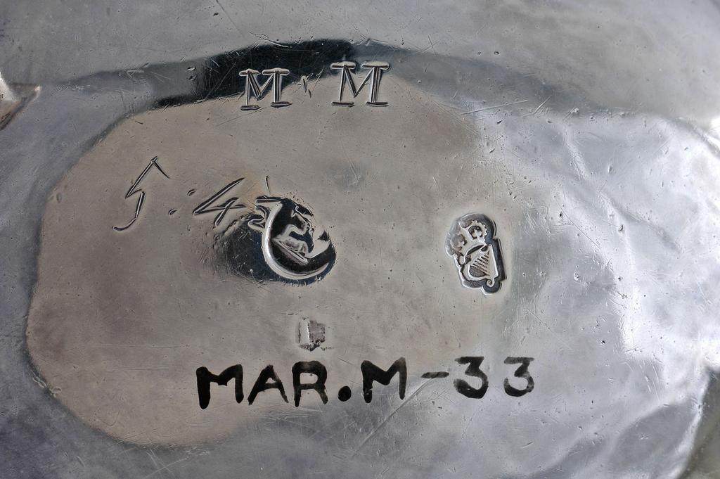 An image of Sauce boat. H?, silversmith, Ireland, Dublin. Oval with wavy edged rim; the sides undecorated; standing on three cast legs with trefoil capitals, knuckles, and hoof feet; with double scroll flying handle, the base scratch engraved with the initials ‘MM’ and ‘5:4½’ for 5 oz 4 ½ dwt. Silver, height, to top of handle, 8.2 cm, width, from lip to handle, 16 cm, weight, overall, 170 g, circa 1760.