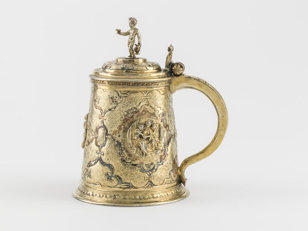 An image of Tankard. SA, silversmith, Augsburg. Flötner, Peter, after (German, c.1485-1546). The sloping cylindrical sides are embossed and chased with an elaborate pattern of straps containing etched Arabesques and three applied cast relief medallions of Charity, Hope and Temperance. The similarly decorated stepped cover is sumounted by a figure of a young Bacchus and has a thumb-piece in the form of a double tailed mermaid. The spreading circular foot and the rim of the neck are decorated with a border of flattened beads. The D-shaped handle is engraved with a border of Arabesques and has an applied acanthus leaf at the top. Silver whole, gold surface (silver-gilt, embossed, chased and etched), height, to top of finial, 17 cm, diameter, base, 11.3 cm, weight, whole, 480 g, circa 1570-1600. Renaissance. Notes: The young Bacchus finial is almost certainly a replacement. The gilding is later. The plaques of Charity, Hope, and Temperance are after plaquettes by a follower of Peter Flötner, after rectangular plaques by Flötner.