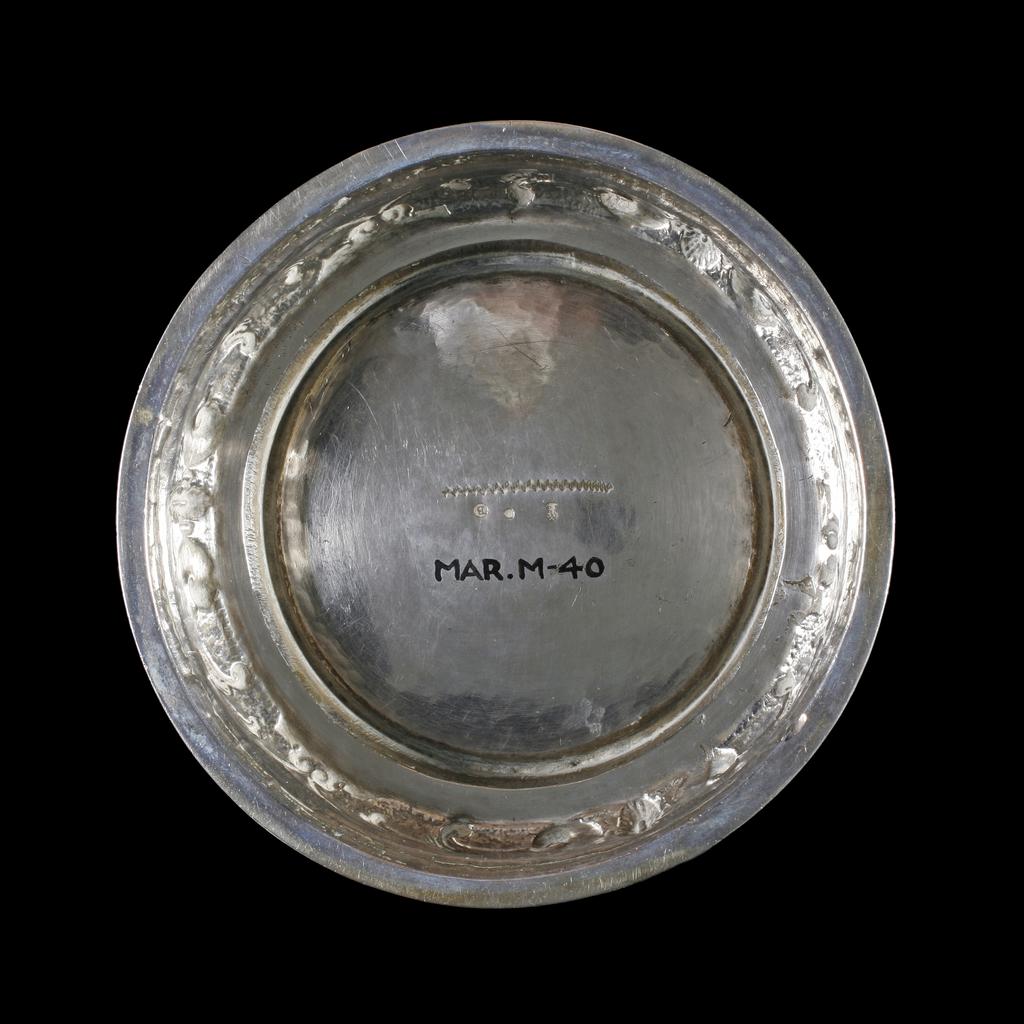 An image of Tankard. Brechtel, Georg, silversmith (active 1594; died 1632, Augsburg). The tall slender body with sloping cylindrical sides is embossed with a formal pattern of strapwork containing scrolls, fruit and flowers on a matted ground. It stands on a slightly domed spreading circular foot. The slightly domed cover is similarly decorated with a baluster knop. The scroll handle has a bi-furcated thumb-piece. Silver-gilt, embossed, cast finial, raised cover, height, to top of finial, 22.6 cm, diameter, base, 13 cm, weight, whole, 785 g, circa 1595-1600. Mannerist.