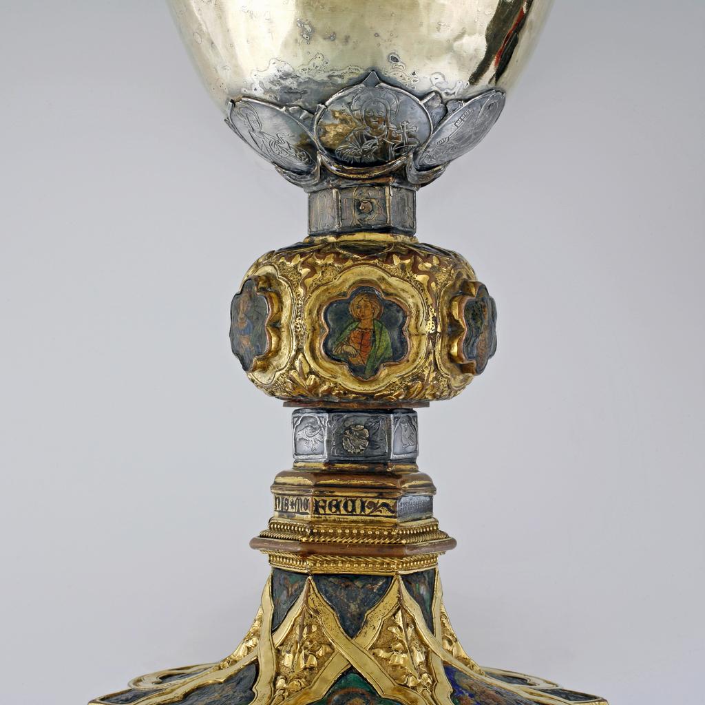 An image of Silver/Church Plate. Chalice. Petruccio Campagnini, Andrea, probably (active Tuscany, Siena, Italy). Set with six silver medallions of Christ, St Peter, St. Paul, St. John, St. Bartholomew and possibly St. Barnabus. Above the knop the stem is engraved with six male busts without nimbi; below the knop the stem is engraved with six birds. At the base of the stem are moulded borders containing a plain band engraved and enamelled with the inscription 'ANDREA * PETRUCI * DE * SENIS * ME *FECI(T). The low copper-gilt trumpet-shaped foot has a shaped circular spreading base with rim of twelve alternating semicicular and pointed lobes. It is set with six applied silver plaques with translucent enamels on sunk relief, representing the Crucifixion with Instruments of the Passion, on either side of which are the Virgin and St. John; on the opposite side are a bishop with mitre and crozier between a male and female saint. Above are smaller shaped triangular plaques enamelled with the heads of angels; and below are lozenge shaped plaques enamelled with a stylised leaf. The base stands on a foot ring decorated with moulded, beaded and dentil borders. Bowl silver-gilt with silver calyx, foot and stem of copper-gilt, decorated with embossing and chasing, and set with silver plaques with basse taille enamelling, height, overall, 19 cm, diameter, base, 12.8 cm, maximum, diameter, rim, 9.9 cm, circa 1370. Late Medieval. Gothic.