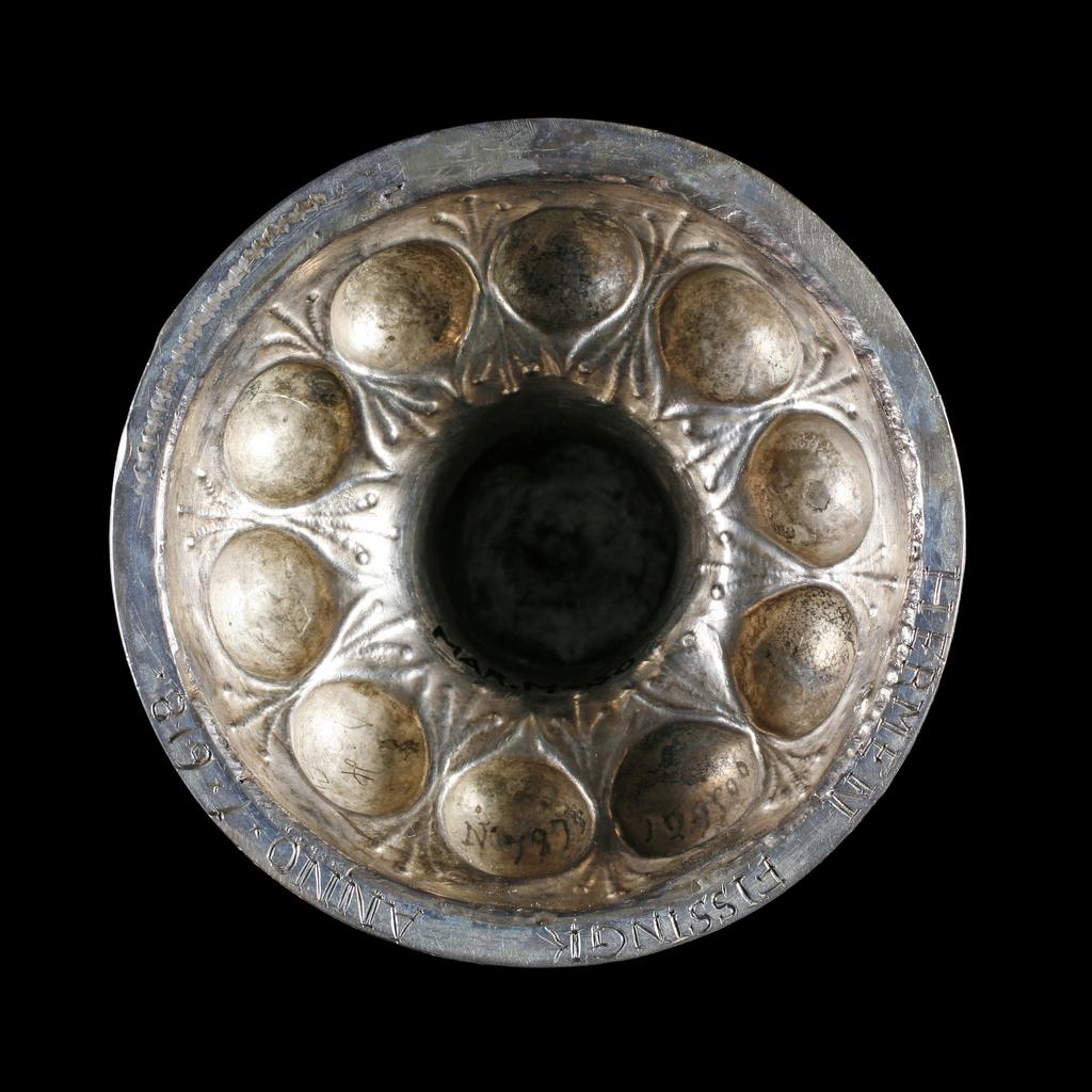 An image of Cup and cover/pineapple cup. Fischer, Franz (silversmith, Nüremberg, surname is also spelt Vischer). Lobed ovoid body and cover supported by a stem in the shape of a tree trunk with figure of a woodman. Silver-gilt; the spreading circular silver-gilt foot is embossed with a ring of lobes round a central dome, which supports the silver stem in the shape of a tree trunk encircled by a creeper, and the figure of an ax-wielding woodman. The ovoid silver-gilt body and interlocking cover are embossed with lobes. The silver finial is formed as a bunch of flowers. Silver and gold, raised and embossed body and foot, cast stem and woodcutter, height, overall, 33.3 cm, diameter, overall, 8 cm, weight, whole, 281 g, 1600-1653. Mannerist.