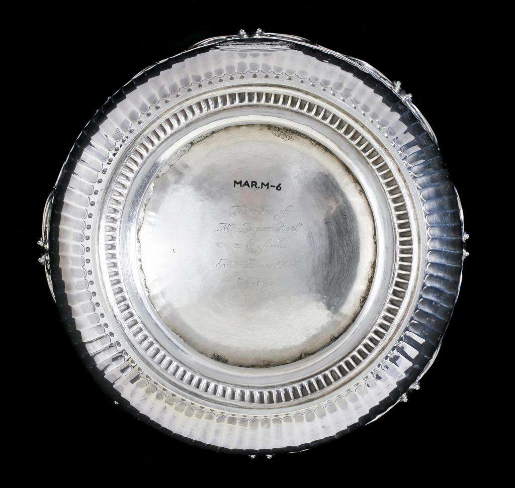 An image of Monteith. Punch bowl. BI or RI, silversmith, England, London. Large hemispherical bowl with removable rim with scroll border. The body of the large hemisperical bowl is embossed with bats-wing fluting. In the front there is an oval cartouche containing a crest within an engraved Baroque border. The bowl stands on a stepped and spreading circular foot with a gadroon border. The removable rim has an applied scroll border, which is decorated with matting and scalework. Beneath this is chased a narrow border of matt scallops and punched flowers. The base is inscribed 'The token of/ Mr. Jasper Roth/ to his friend/ Aldn. James Clark'. Silver, raised, embossed, chased, and engraved, height, to rim, 23.7 cm, diameter, across rim, 33.5 cm, 1707-1708. Late 17th or early 18th century.