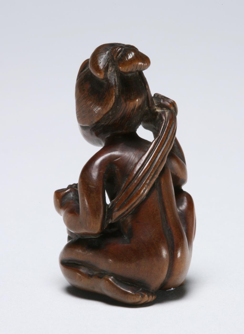 An image of Netsuke. A naked woman crouched at a tub, washing her back. Unknown maker, Japan. Inscription: signature inlaid with mother of pearl; illegible. Wood, mother-of-pearl, height 4.5 cm. Acquisition Credit: Marlay Bequest.