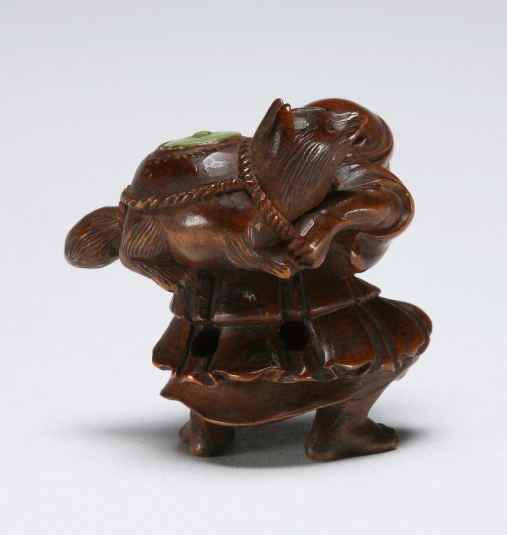 An image of Netsuke. A man carrying on his back a badger which is transforming itself in to a teapot. Minkoku (Japanese). Wood, with stained ivory detail, height 3.5 cm. Acquisition Credit: Marlay Bequest.