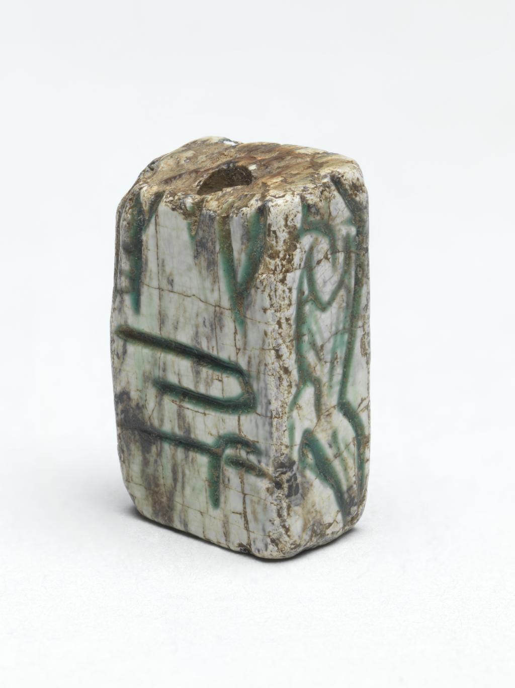 An image of Plaque or amulet/jewellery. Magic rod fragment? Rectangular, inscribed on four sides. Depth, 0.007 m, length 0.018 m, width 0.0105 m. Egyptian.