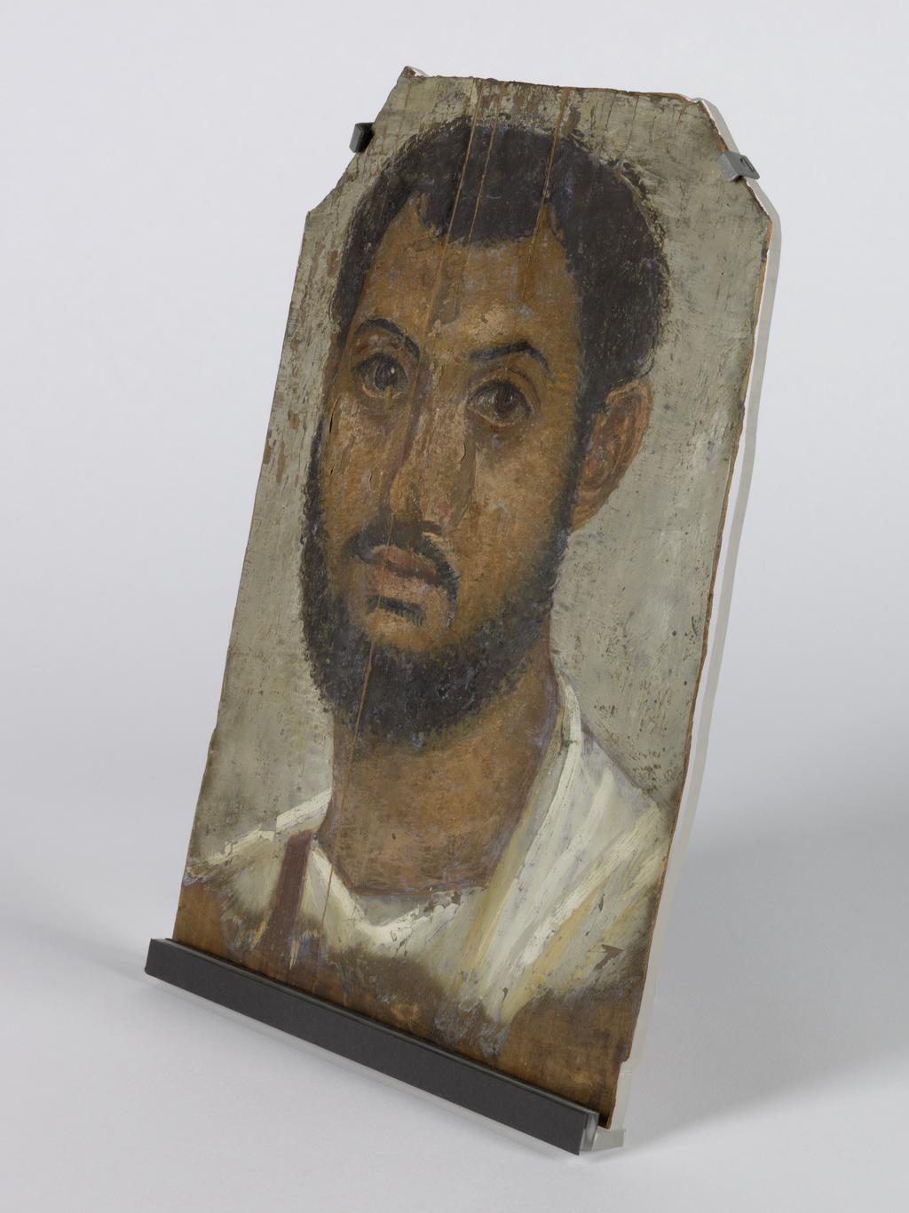 An image of Mummy trappings. Mummy portrait of bearded man. Production Place: Egypt. Find Spot: Negatine-Ella, Egypt or Hawara. Wood, painted, height 32.5 cm, width 22.5 cm, 100-150. Middle Roman.