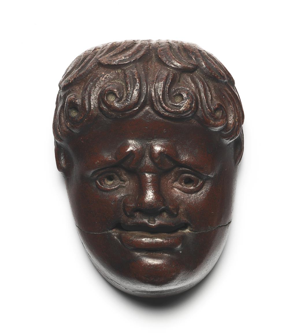 An image of Mask of a New Comedy Youth. Coffin attachment. Moulded, porphyry (imitation), length 6.7 cm, width 4.8 cm, circa 50-100 AD. Egyptian, Roman period.